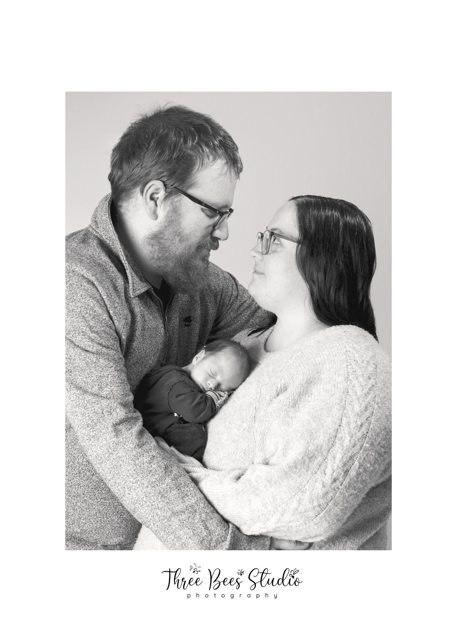 Black and white family portrait with newborn in intimate studio setting.