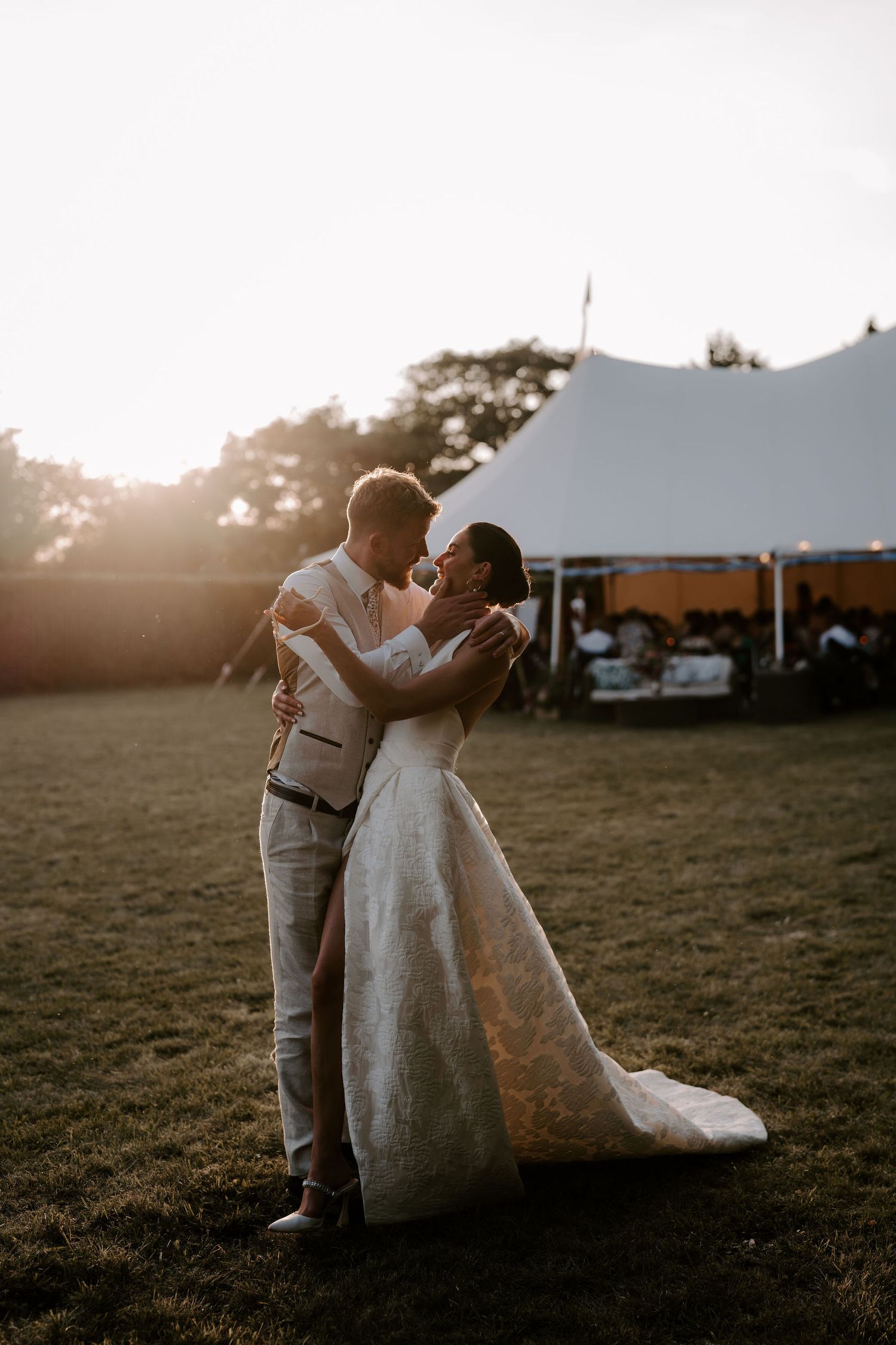 groom pulling bride in for a kiss on lawn outside marquee wedding in islip in oxfordshire