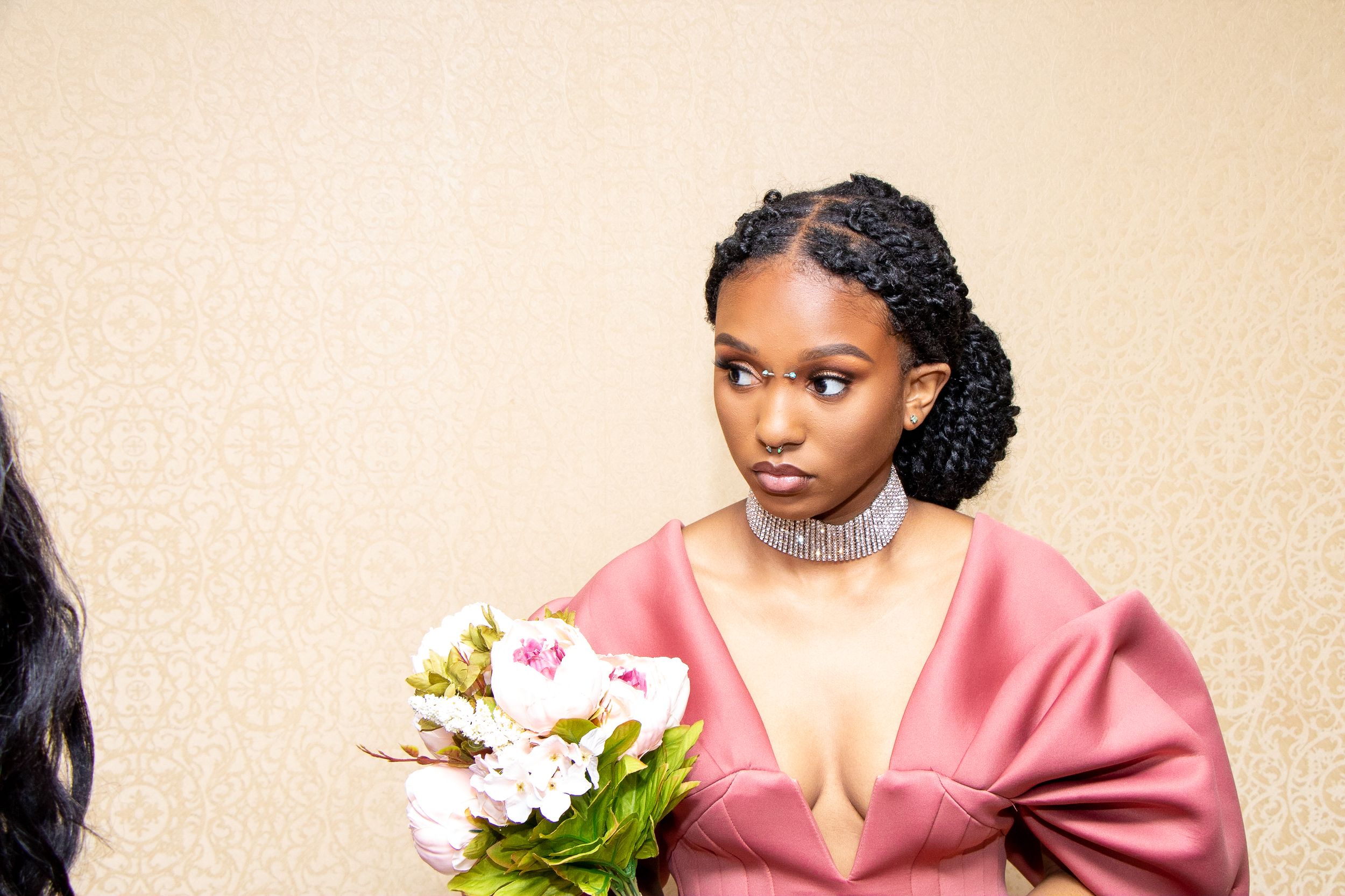 Portrait of someone wearing pink satin dress and crystal choker holding white flowers.