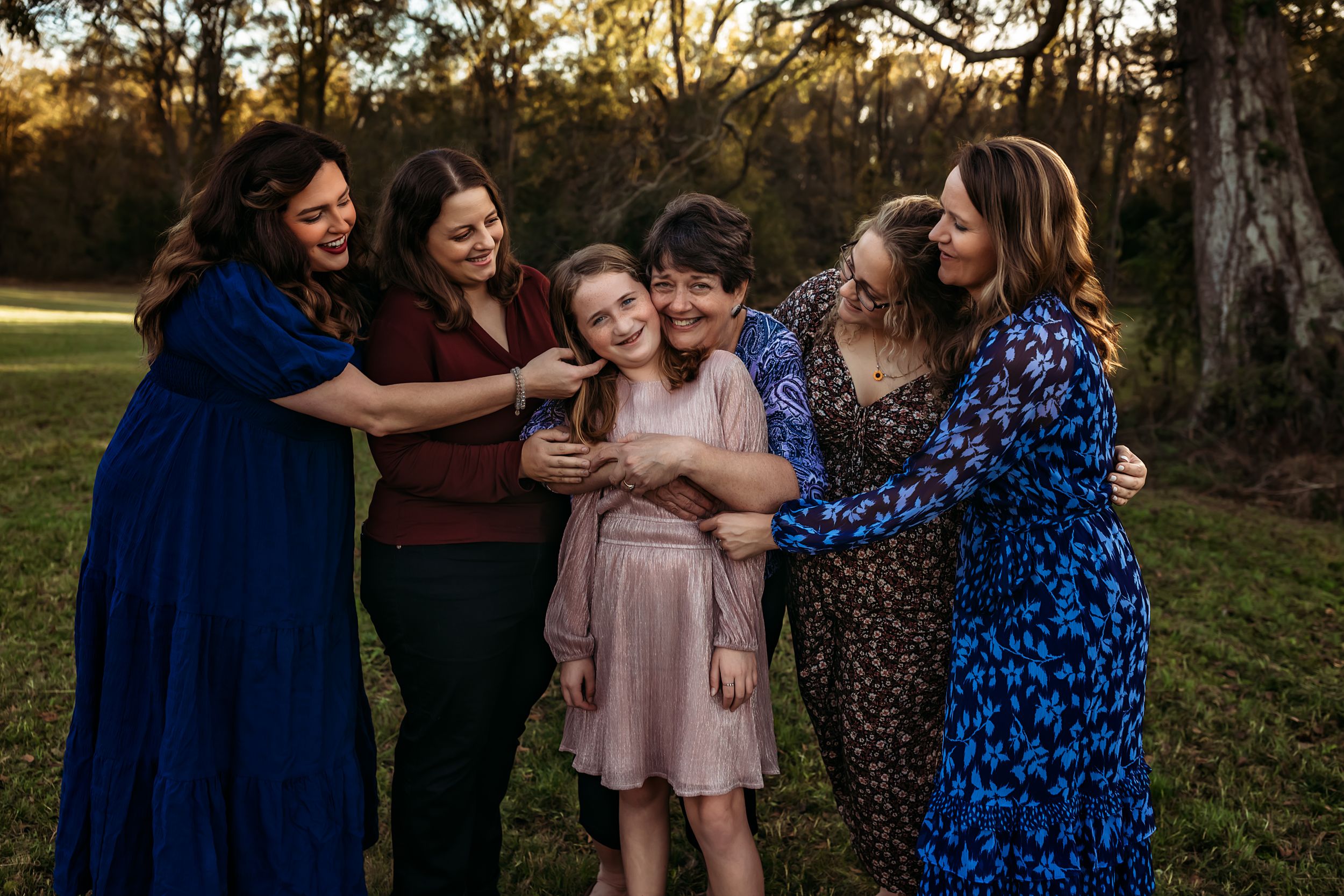 Group of people sharing laughter and embraces under moss-draped trees at sunset.