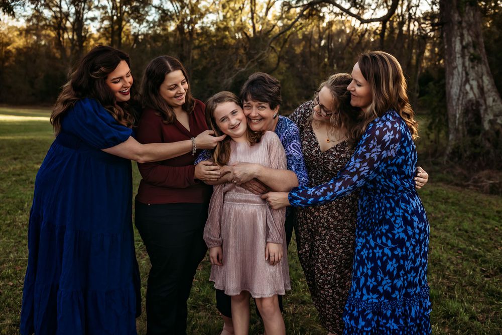 Group of people sharing laughter and embraces under moss-draped trees at sunset.