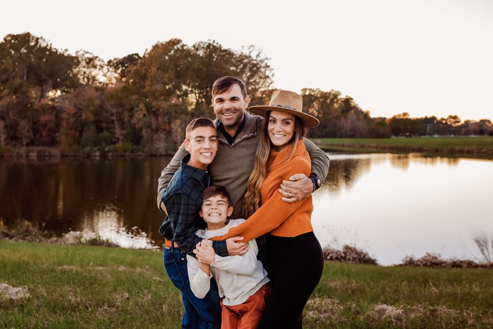 Family of four poses together by a tranquil lake during golden hour.
