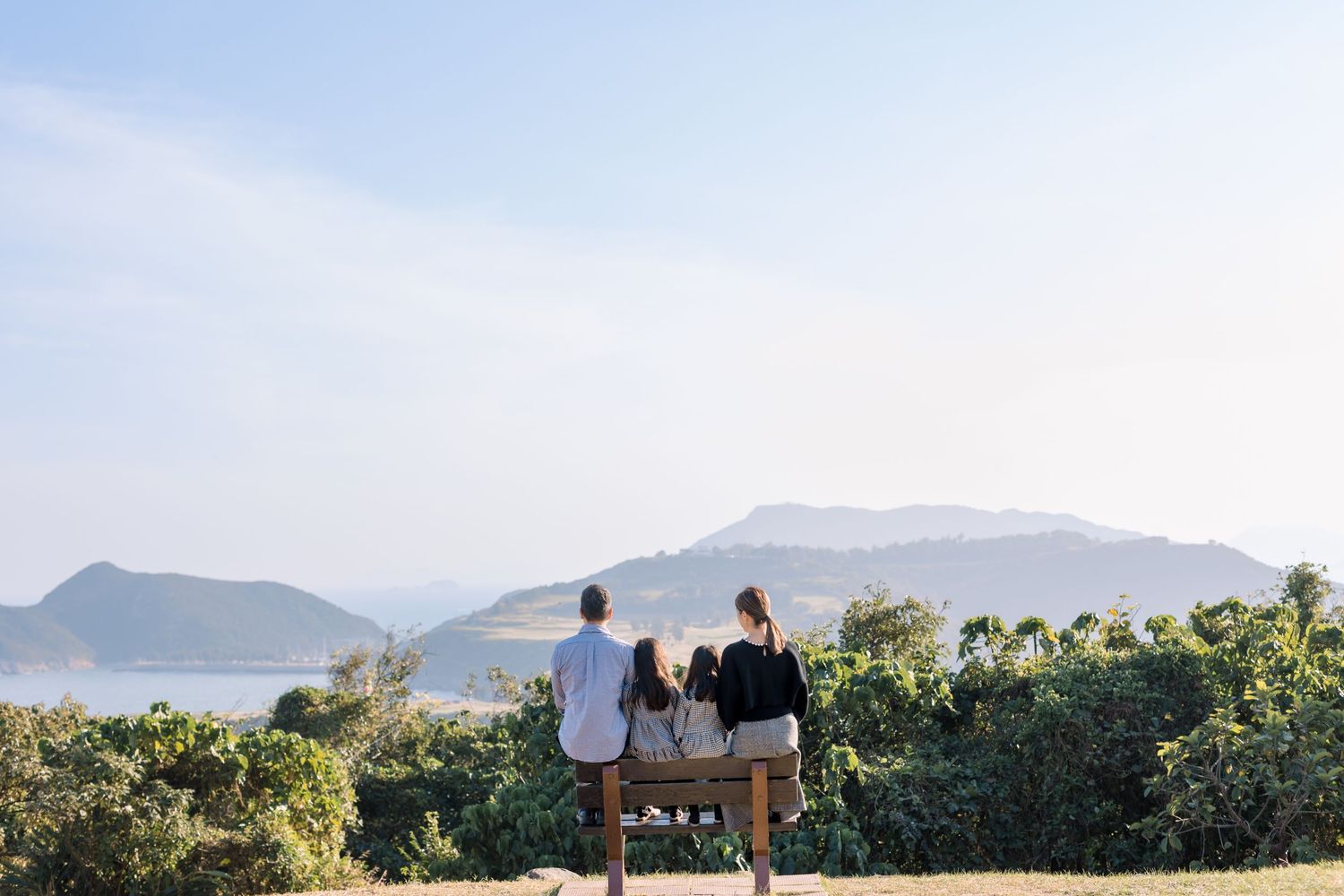 Couple sitting on bench overlooking mountain and ocean landscape at sunset.
