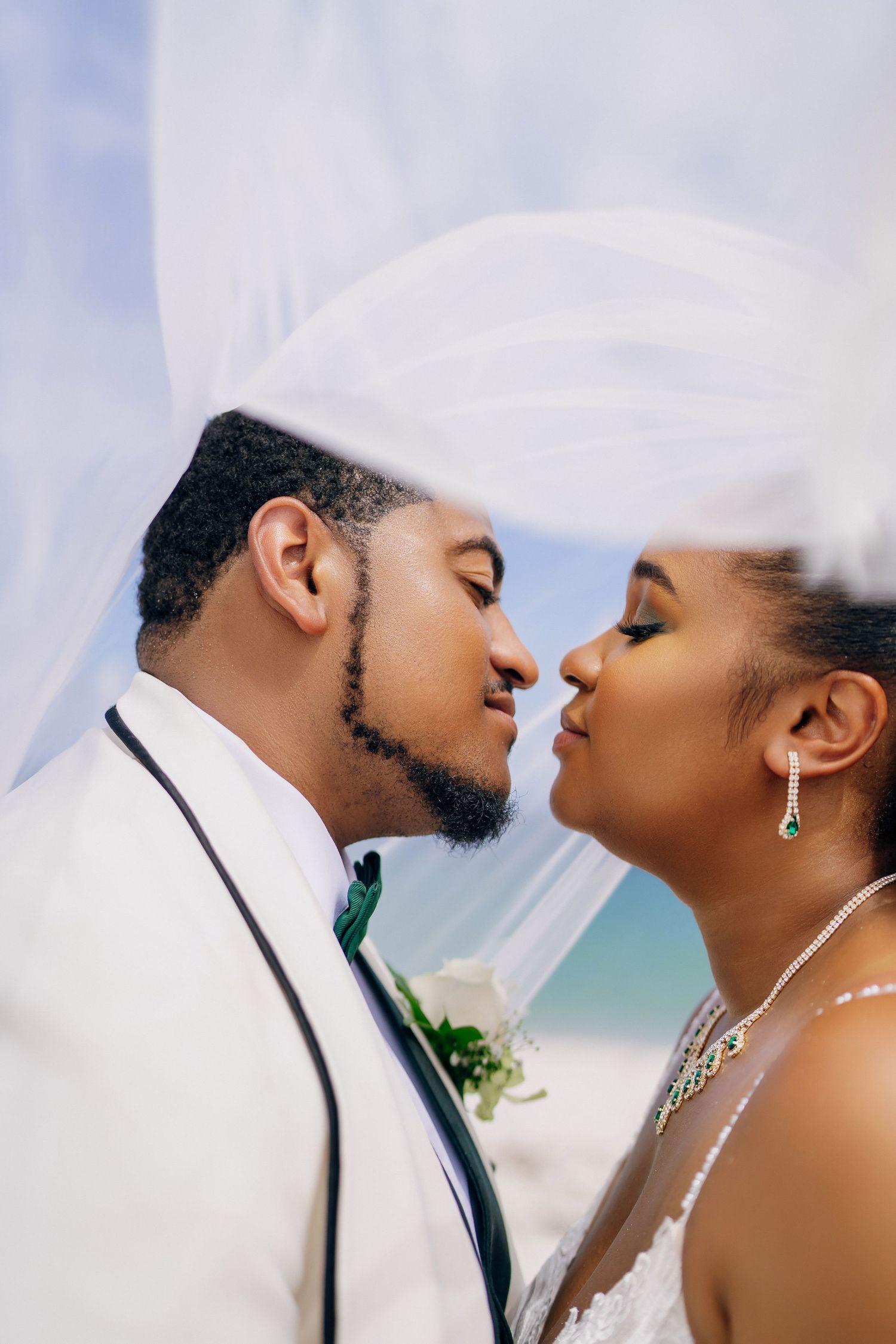 Romantic wedding portrait through flowing veil with sky background.