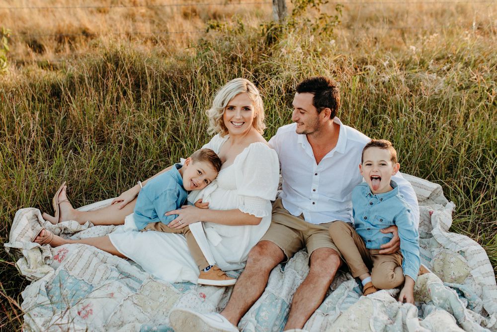 Family sitting together on white blanket in field during golden hour.