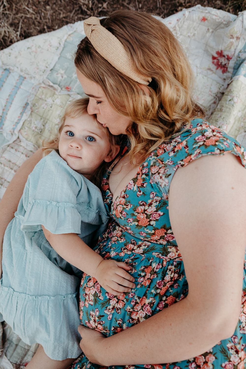 A tender moment between parent and child wearing floral and blue dresses while resting on a blanket outdoors.