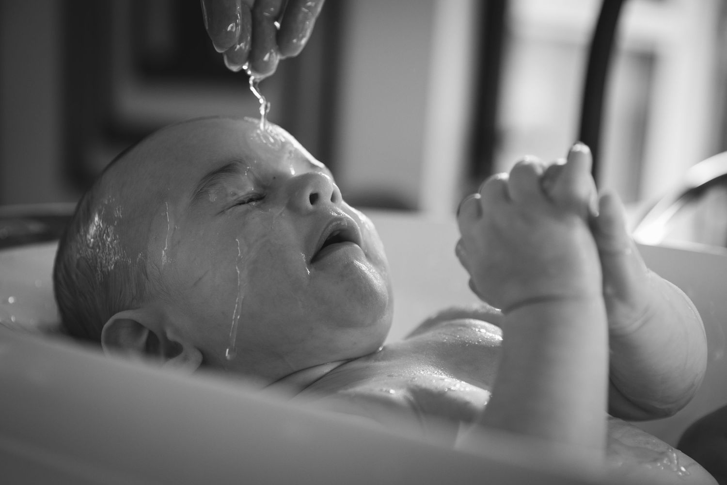 Close up black and white photo of baby during bath time with water droplets.