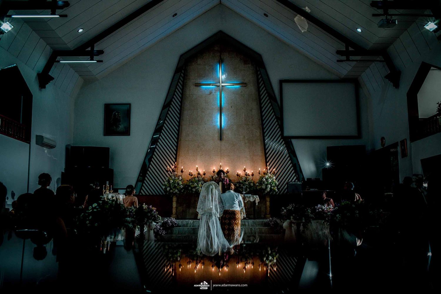 Dramatic evening wedding ceremony in church with illuminated cross and candles creating ambient lighting.
