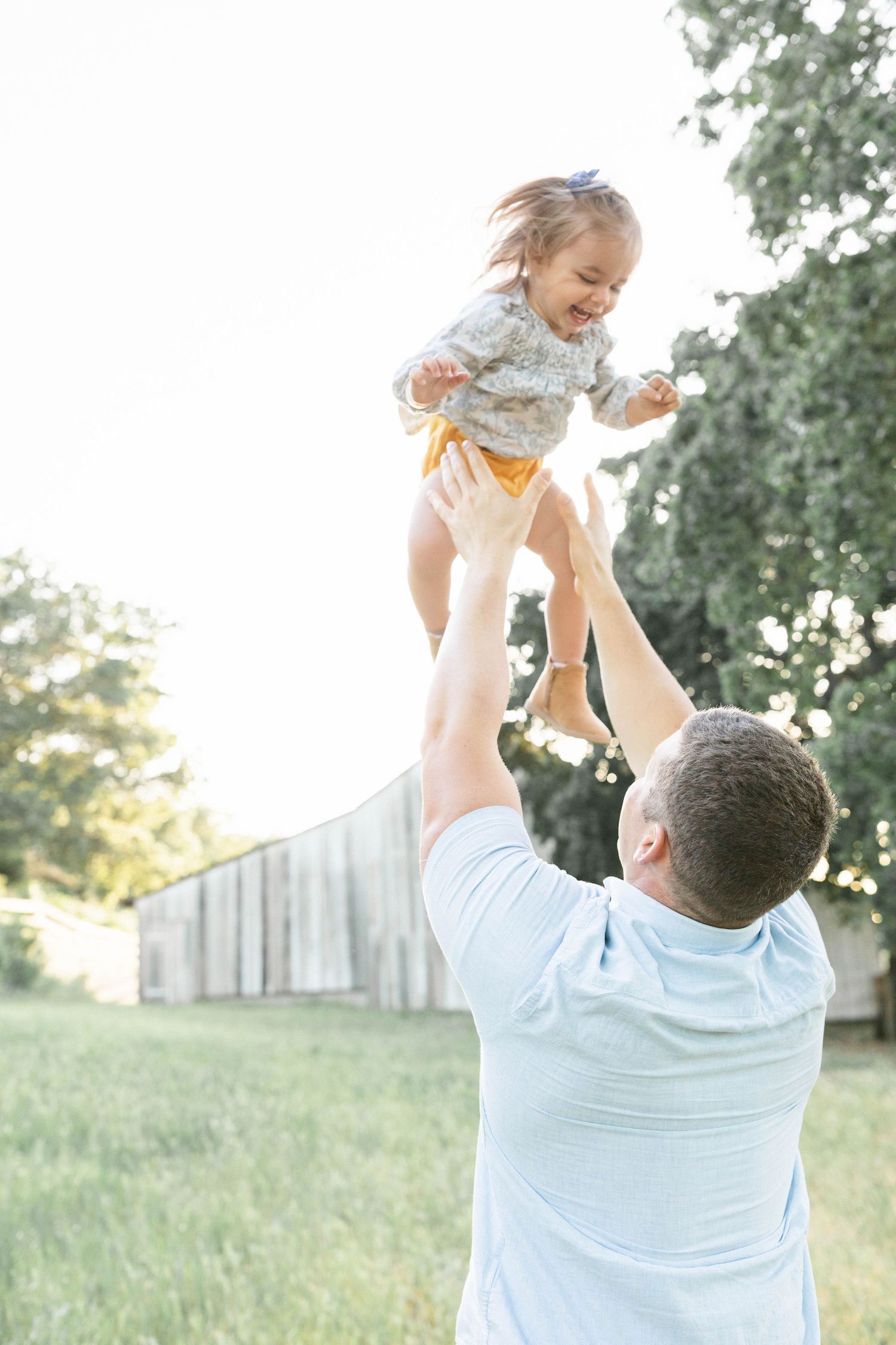 A joyful moment captured as a small child is lifted high into the air on a sunny day.Captured by Chelsee Rawe Photography