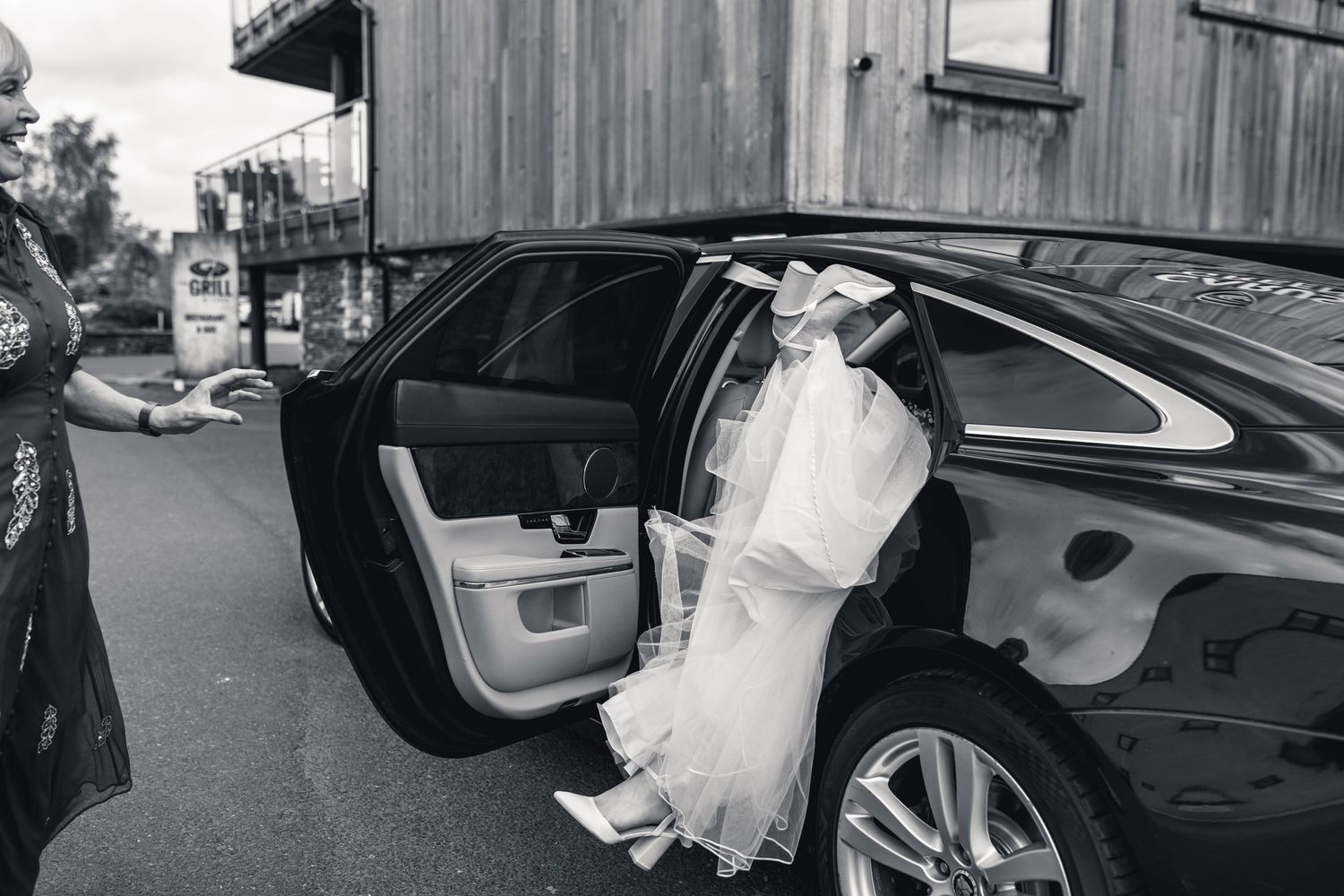 Black and white photo of someone in a wedding dress getting into a luxury car.