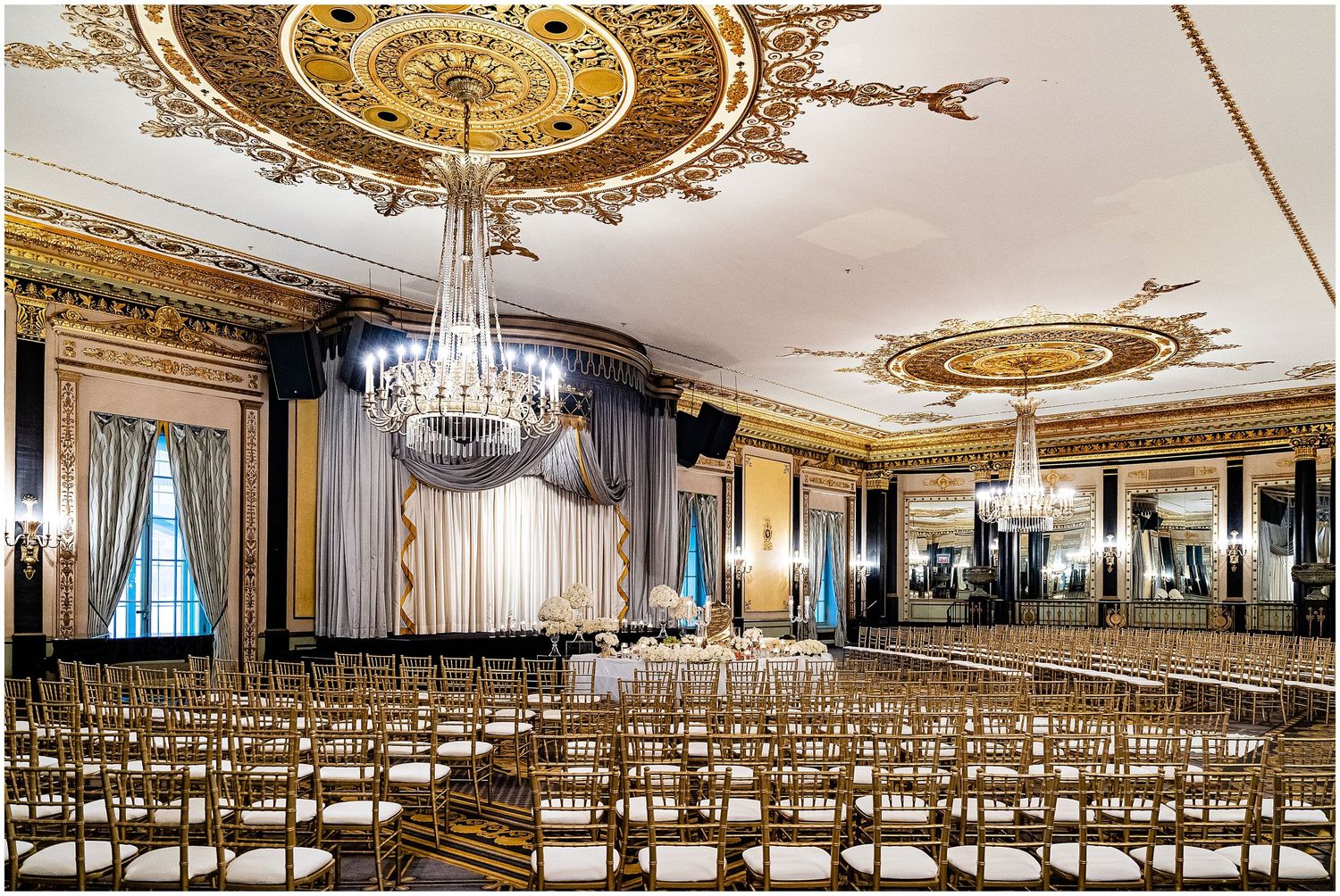 Grand ballroom with gilded ceiling medallions and crystal chandeliers set up for a wedding ceremony.