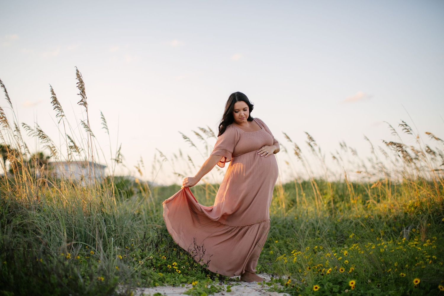 Person in flowing maxi dress twirling in field of tall grass at sunset.