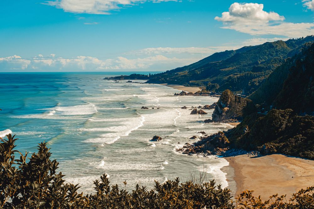 Aerial view of rugged coastline along New Zealands Pacific Coast Highway with sandy beaches and dramatic cliffs.