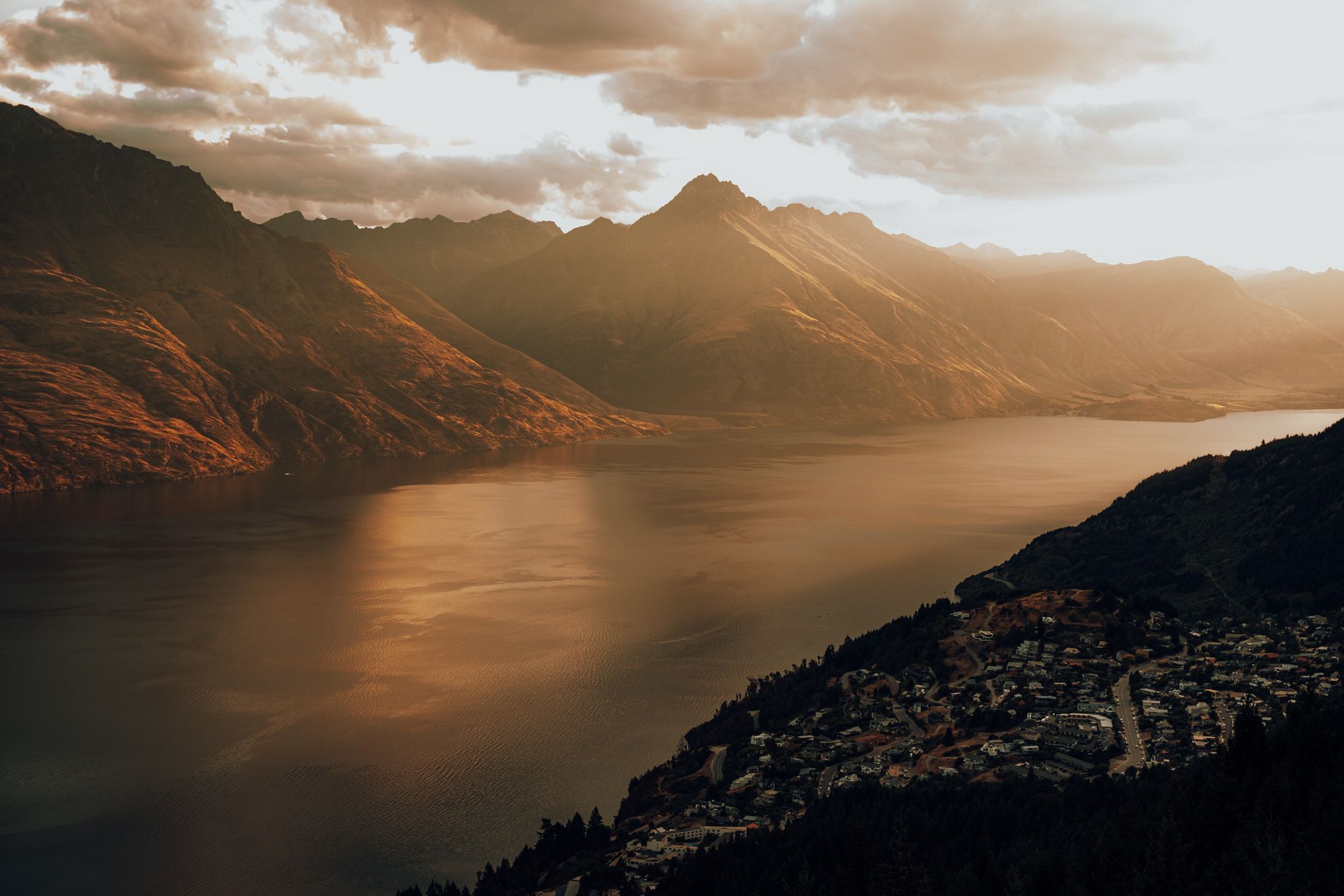 Aerial view of Queenstown, New Zealand with dramatic sunset light over Lake Wakatipu and surrounding mountains.