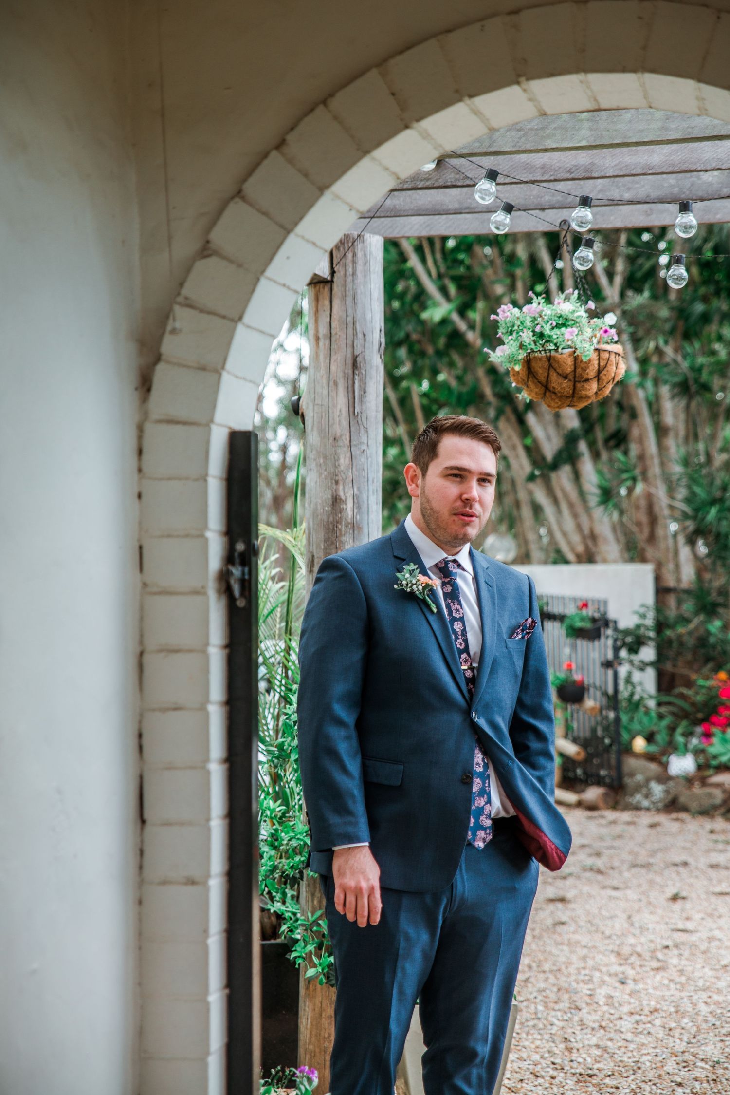 Elegant navy suit under white stone archway in garden setting.