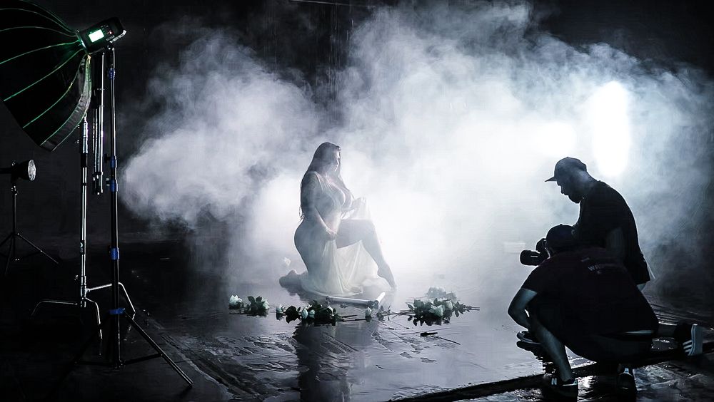 Dramatic photo shoot setup with fog and silhouetted figures in a dark studio setting.