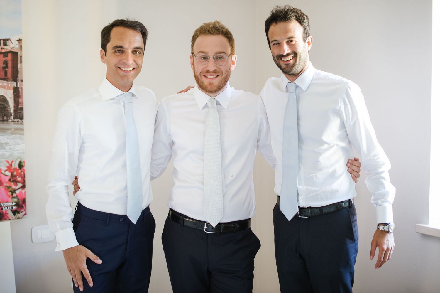 Three people in white shirts and formal attire smiling in a bright interior space.