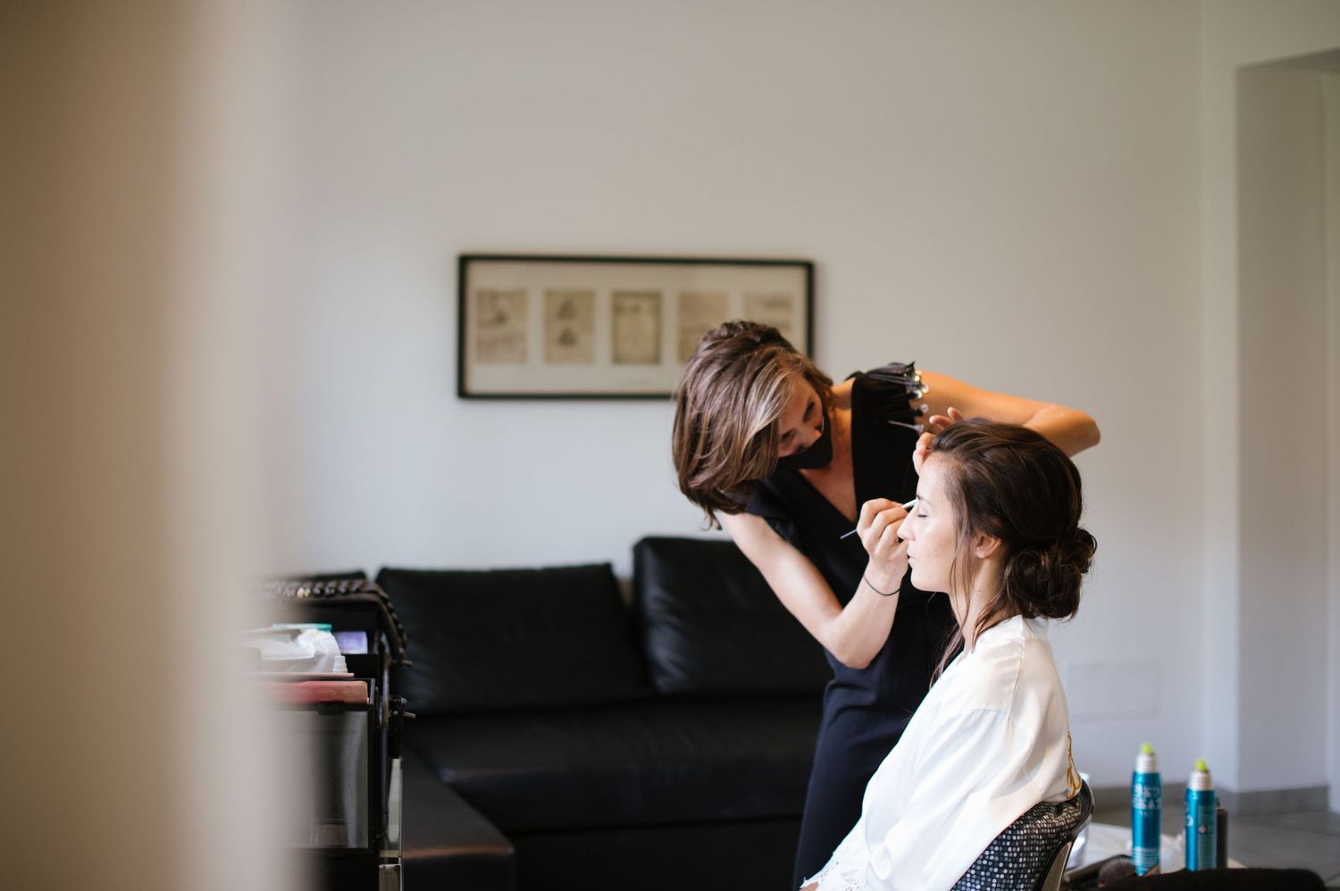 A stylist works on arranging someone's hair in a bright interior setting.