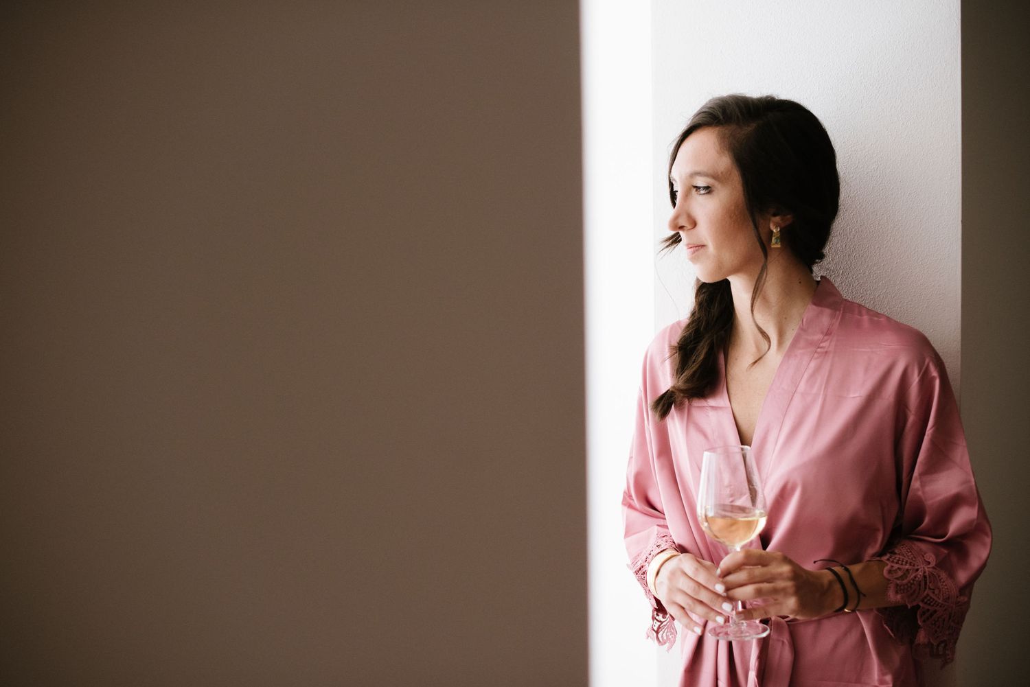 Side profile view of person in pink robe gazing through window during wedding preparation.