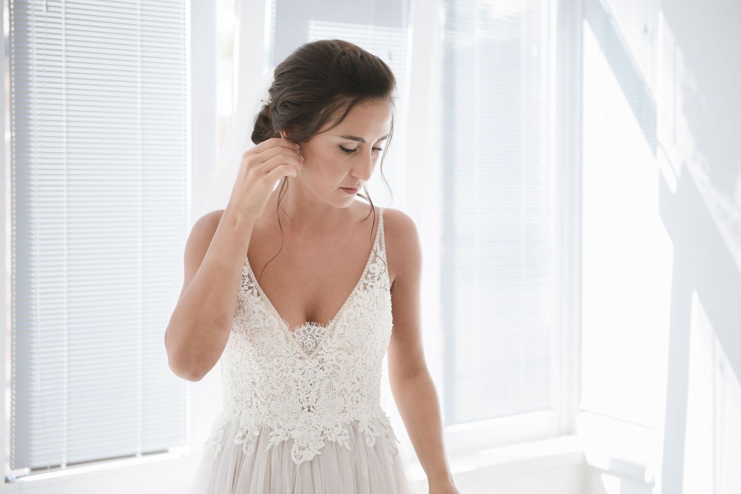 A romantic wedding dress with delicate lace bodice and spaghetti straps shown in a bright white room.