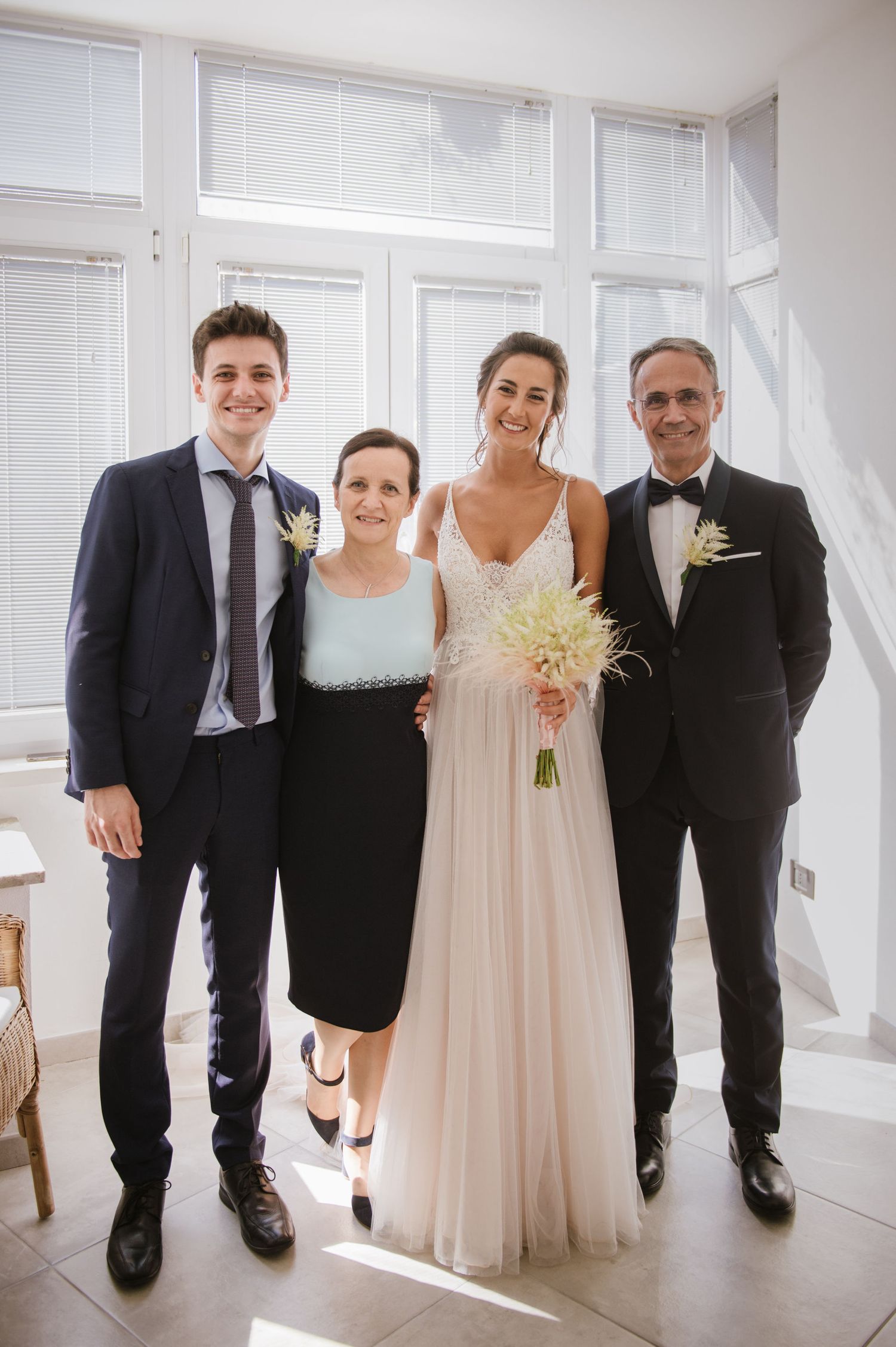 A formal wedding party portrait in a bright modern interior with white windows.