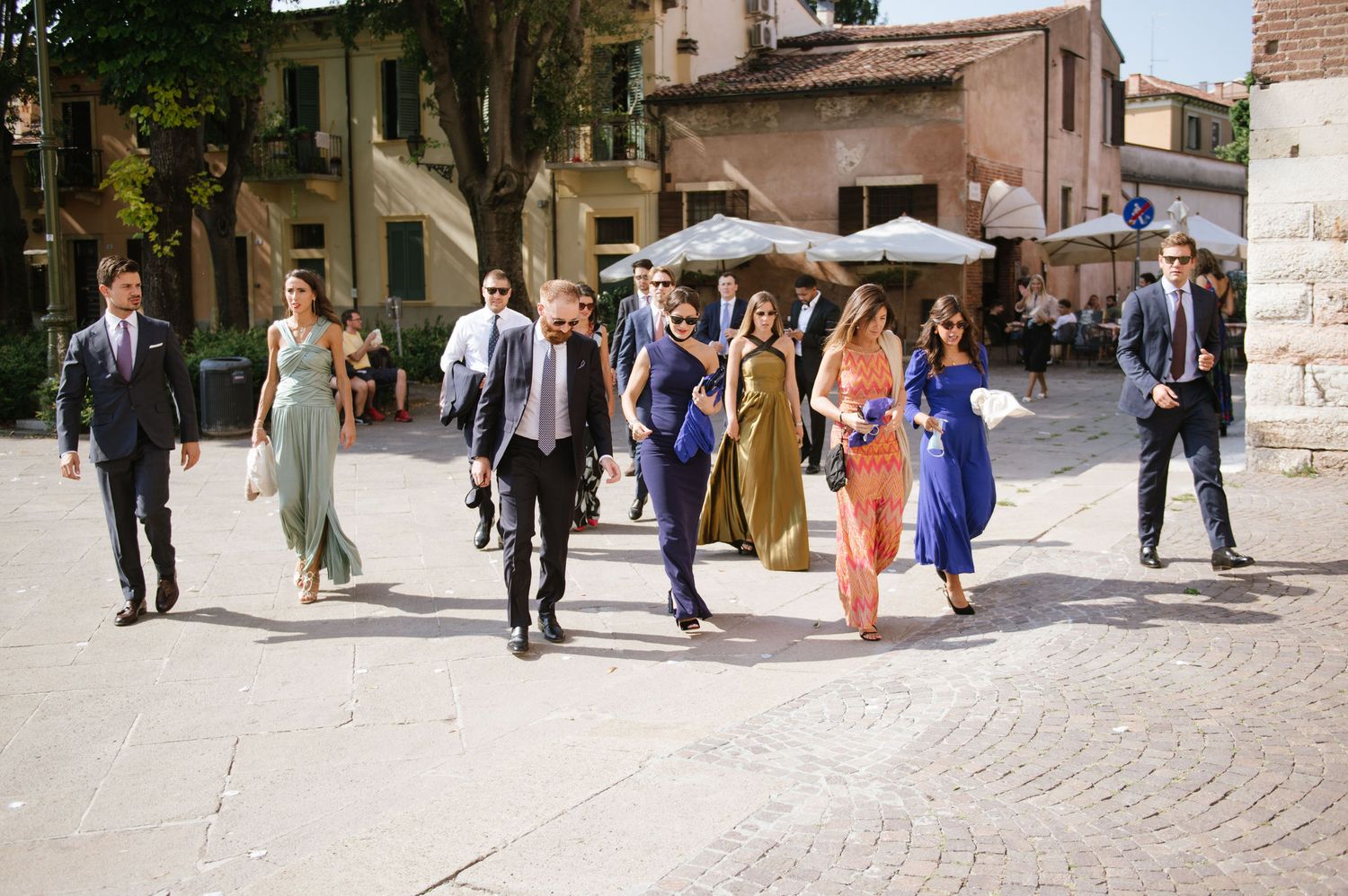 Wedding party and guests walking together through an Italian village street.