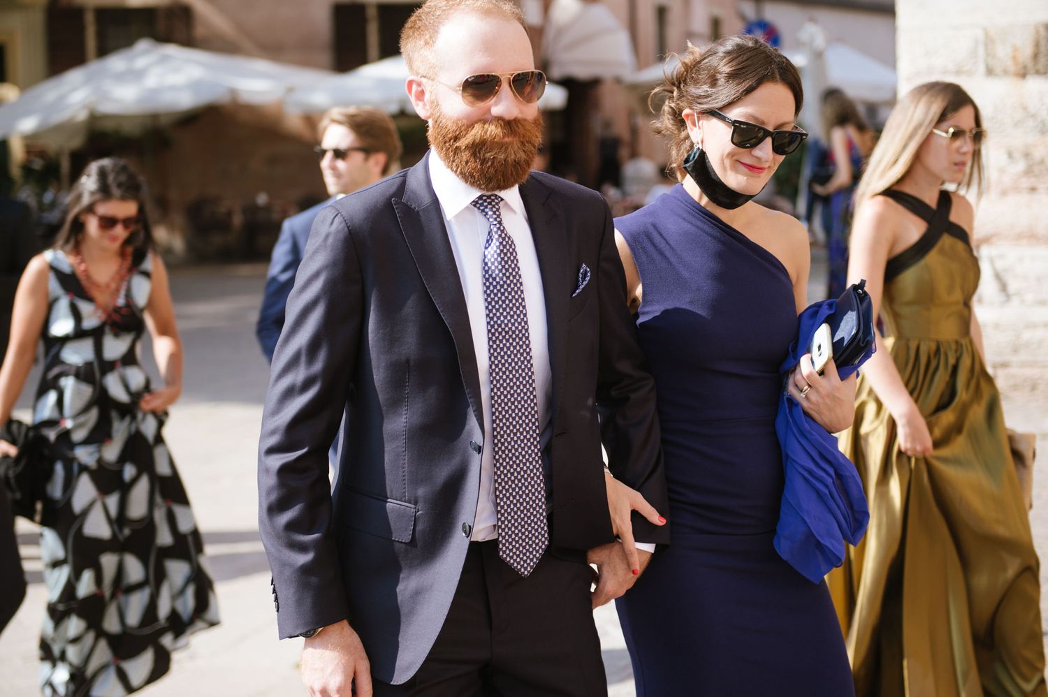 Wedding guests in formal attire walking through a European city street.