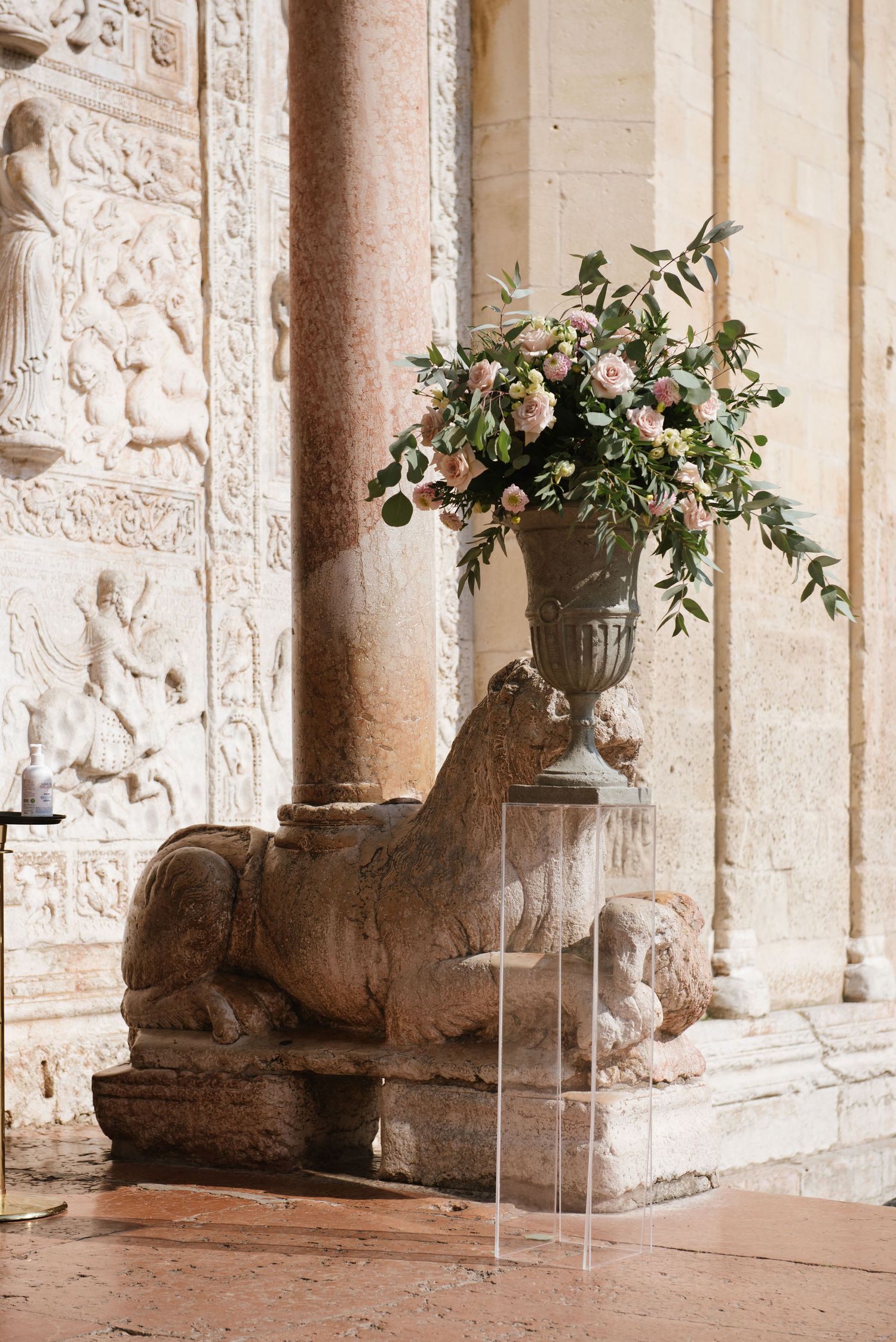 An ornate stone sculpture of a resting lion with a decorative floral arrangement in a classical urn above it.