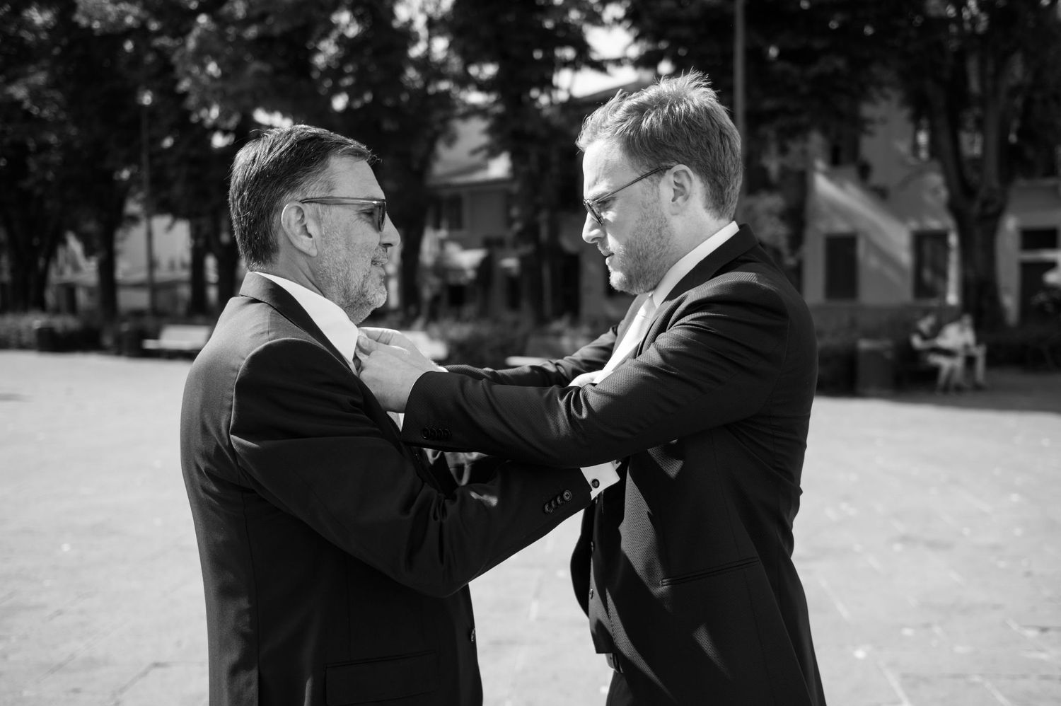 Black and white photo of two men adjusting formal wear before a wedding.