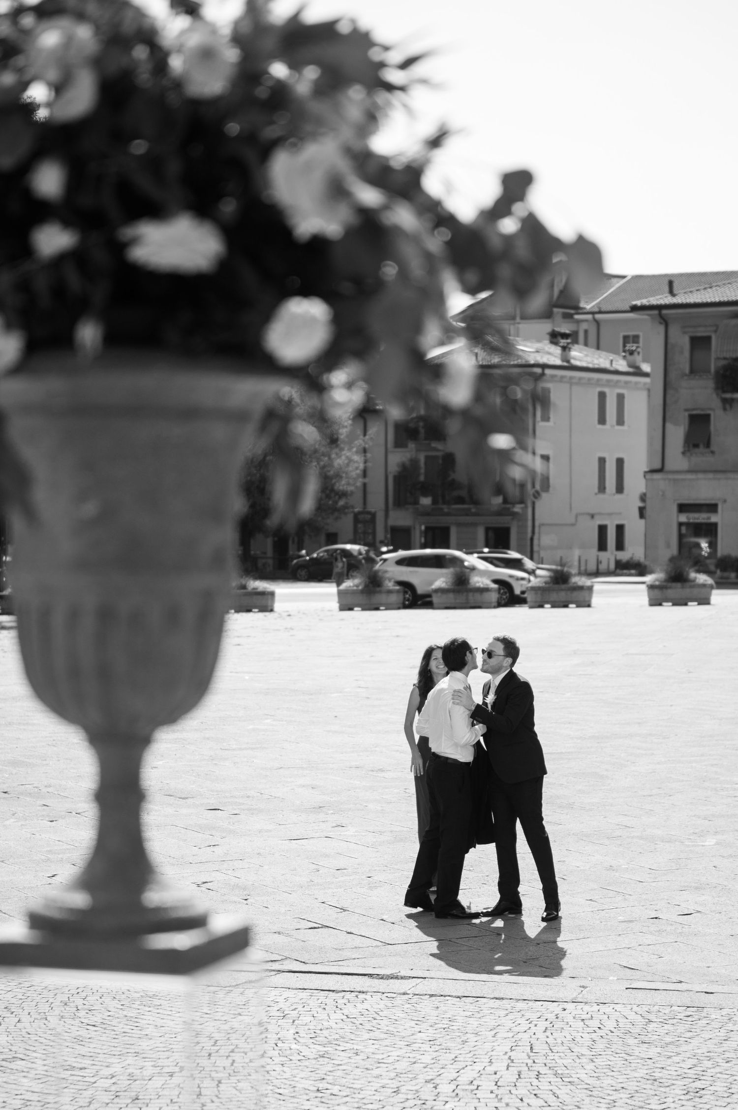 A romantic couple embracing in a plaza, photographed in black and white with a decorative urn in the foreground.