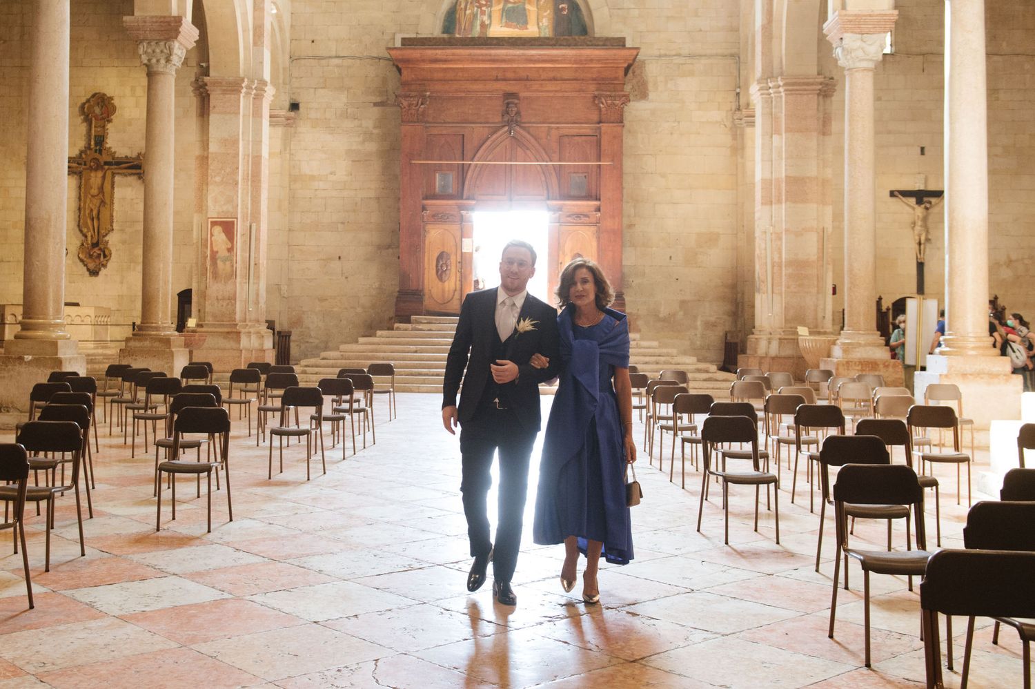 A couple walking through a grand historic church interior with rows of empty chairs.