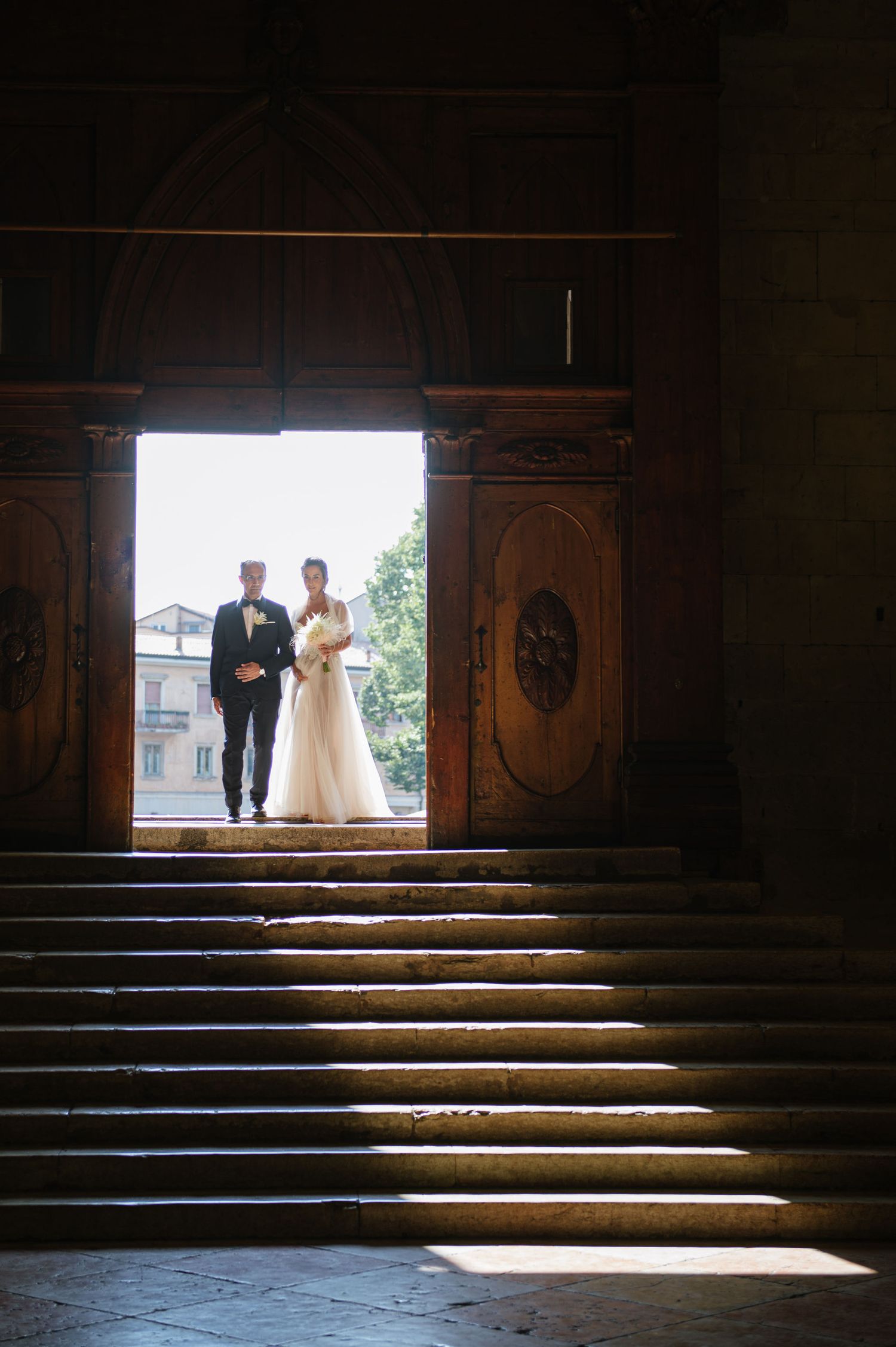 A wedding couple silhouetted in a grand doorway with dramatic stairs and lighting.