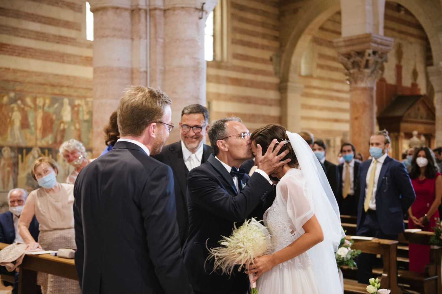 Wedding ceremony in progress inside an ornate Italian church with striped marble walls and frescoes.