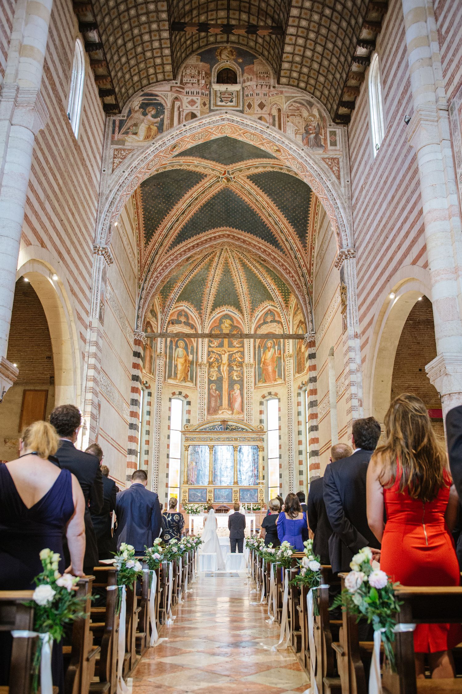 Interior of Italian church with vaulted ceiling, striped marble columns and religious frescoes during wedding ceremony.