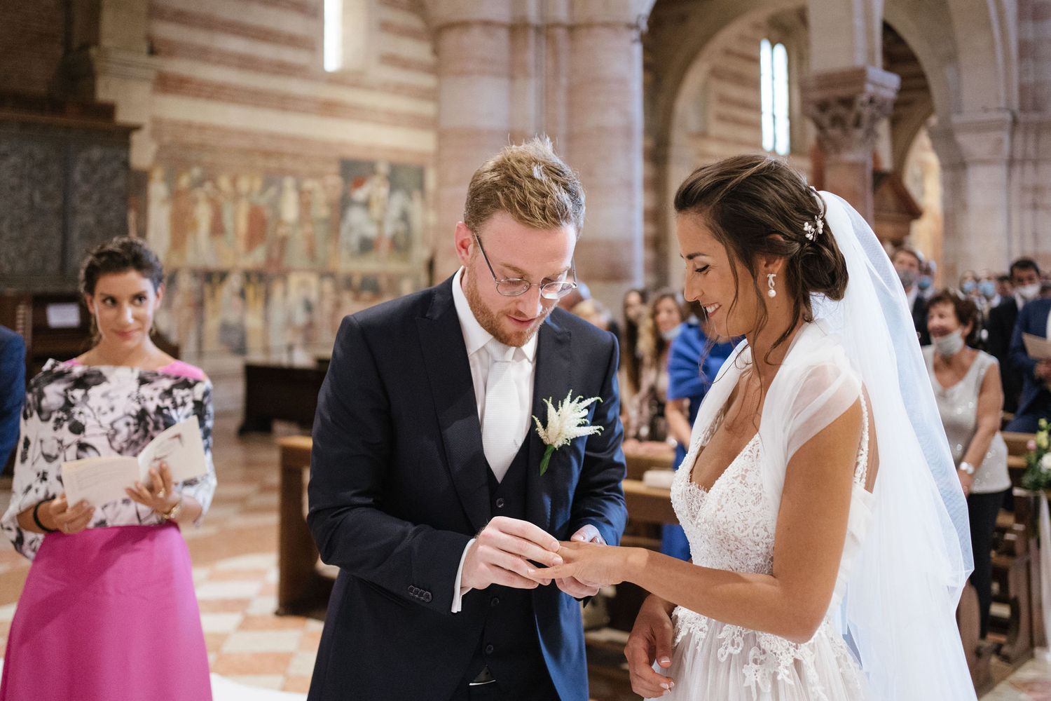 Wedding ring exchange during ceremony in ornate Italian church with guests watching.
