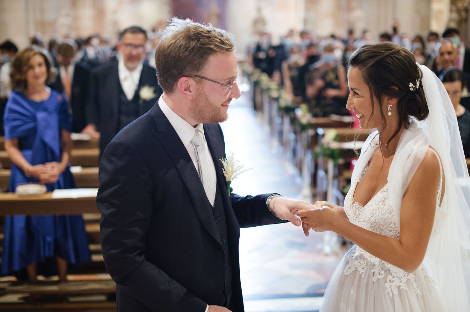 Couple exchanging rings during wedding ceremony in historic Italian church with striped marble walls.