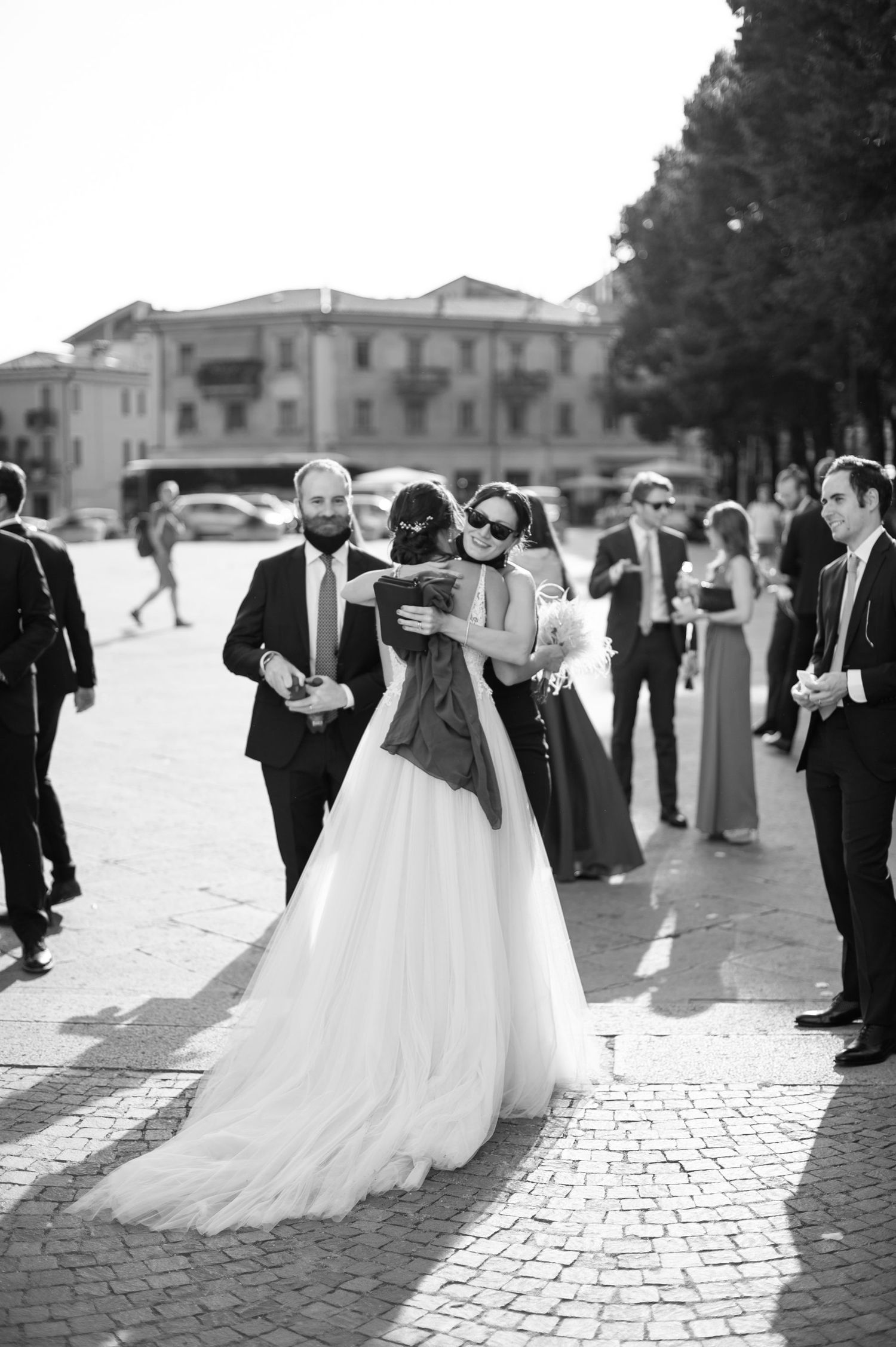 Black and white photo of wedding guests gathered on a cobblestone street in front of Italian architecture.