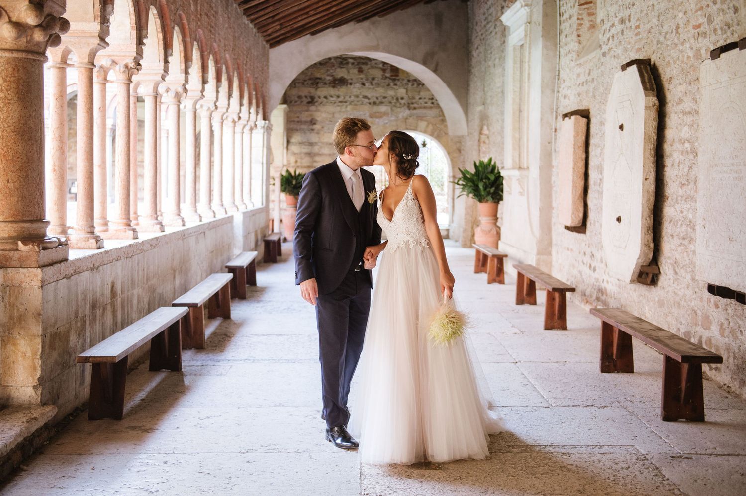 Wedding couple walking through a beautiful medieval cloister with stone columns.