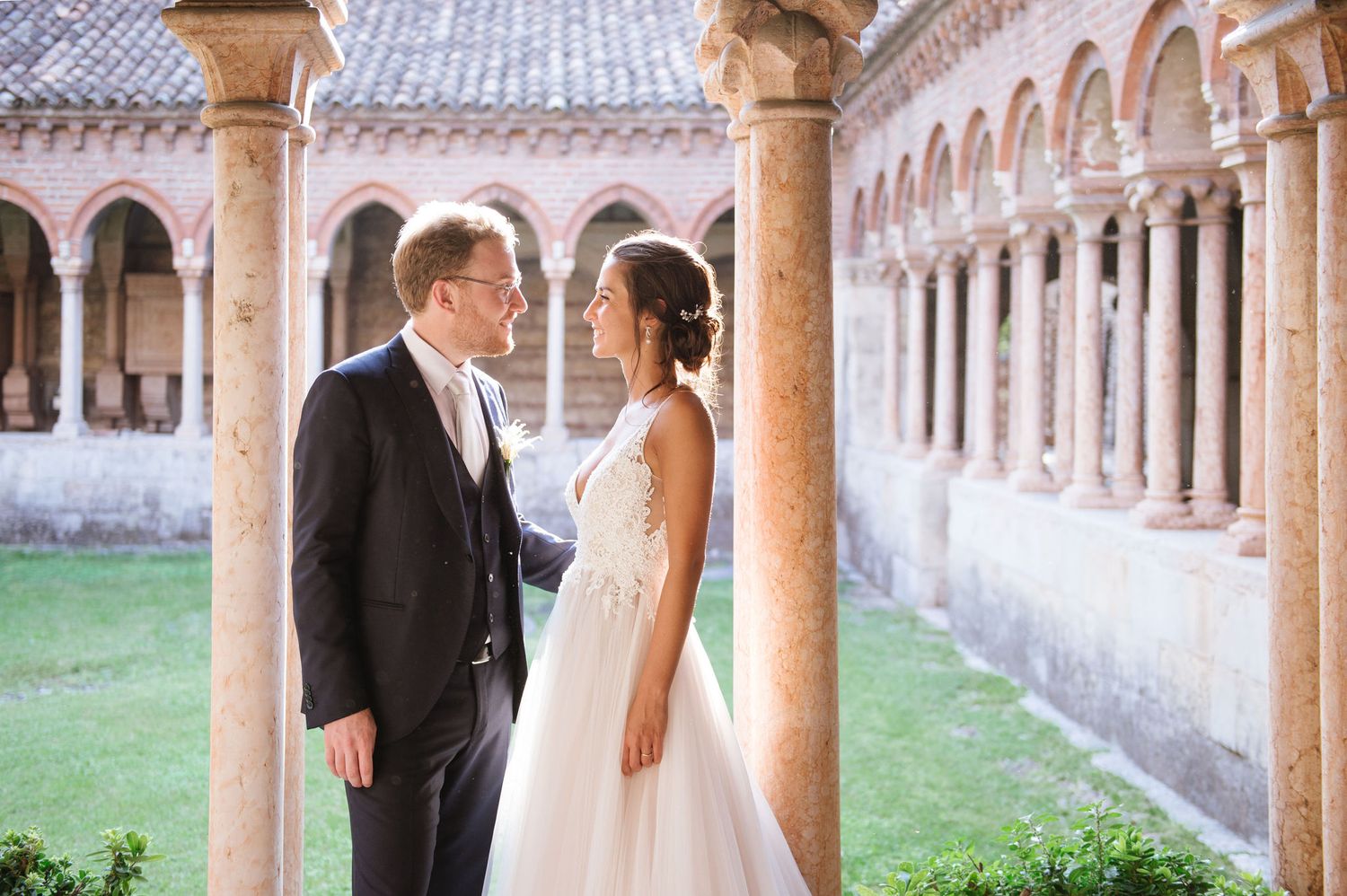 Romantic wedding portrait in a historic courtyard with stone arches and columns.