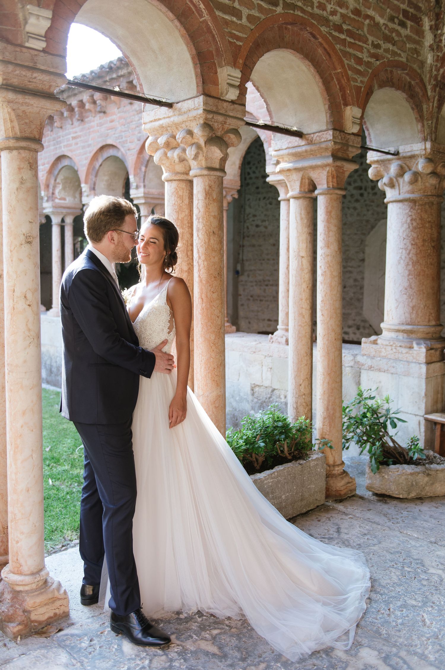 Romantic wedding photo taken in an ancient cloister with brick arches and stone columns.