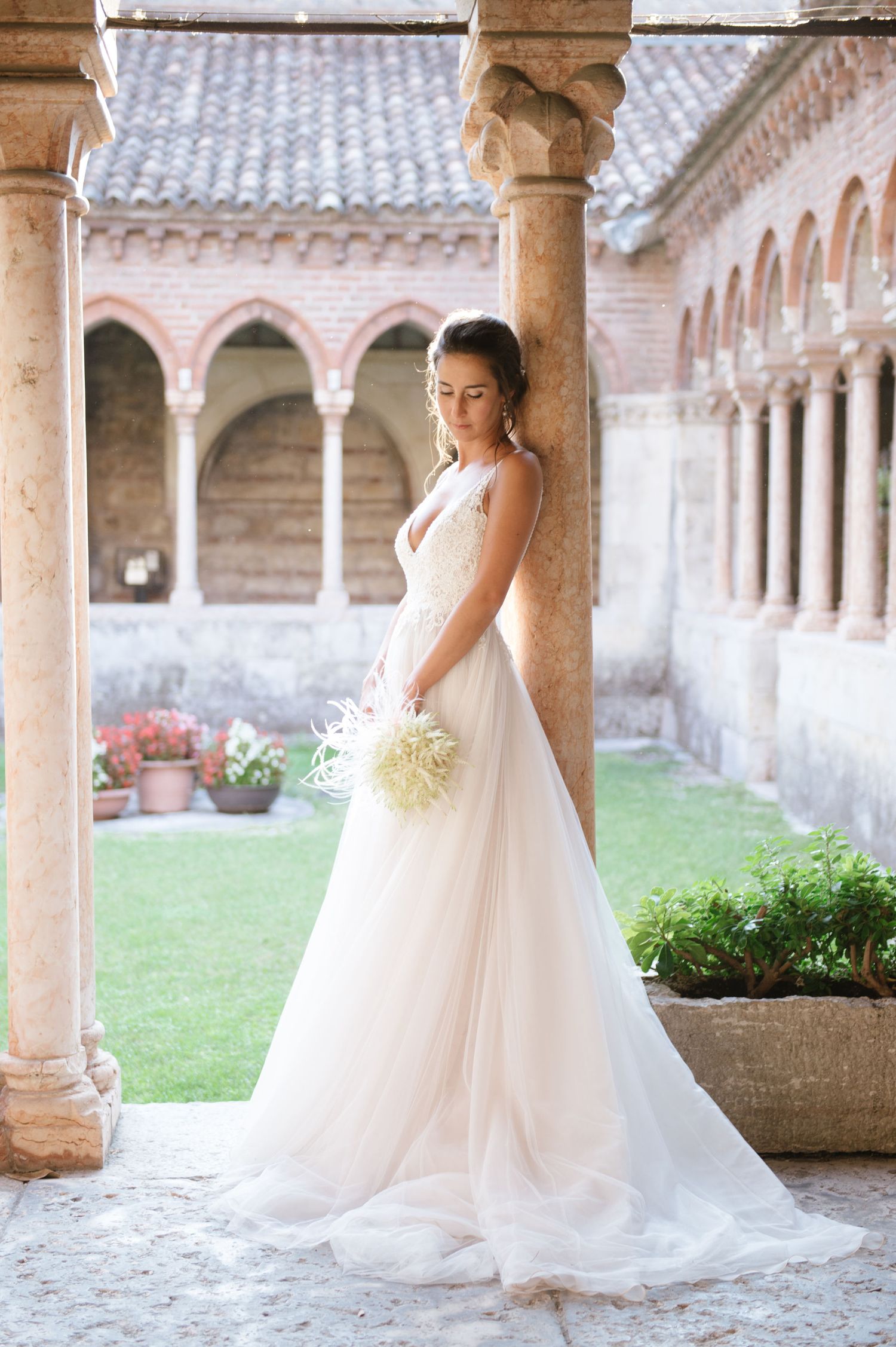 Elegant wedding dress flowing in a medieval courtyard with stone colonnade.