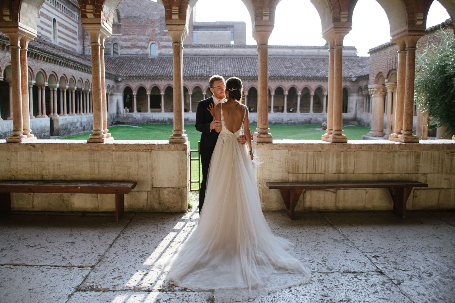 Wedding couple poses in medieval courtyard with ornate stone columns and arches.