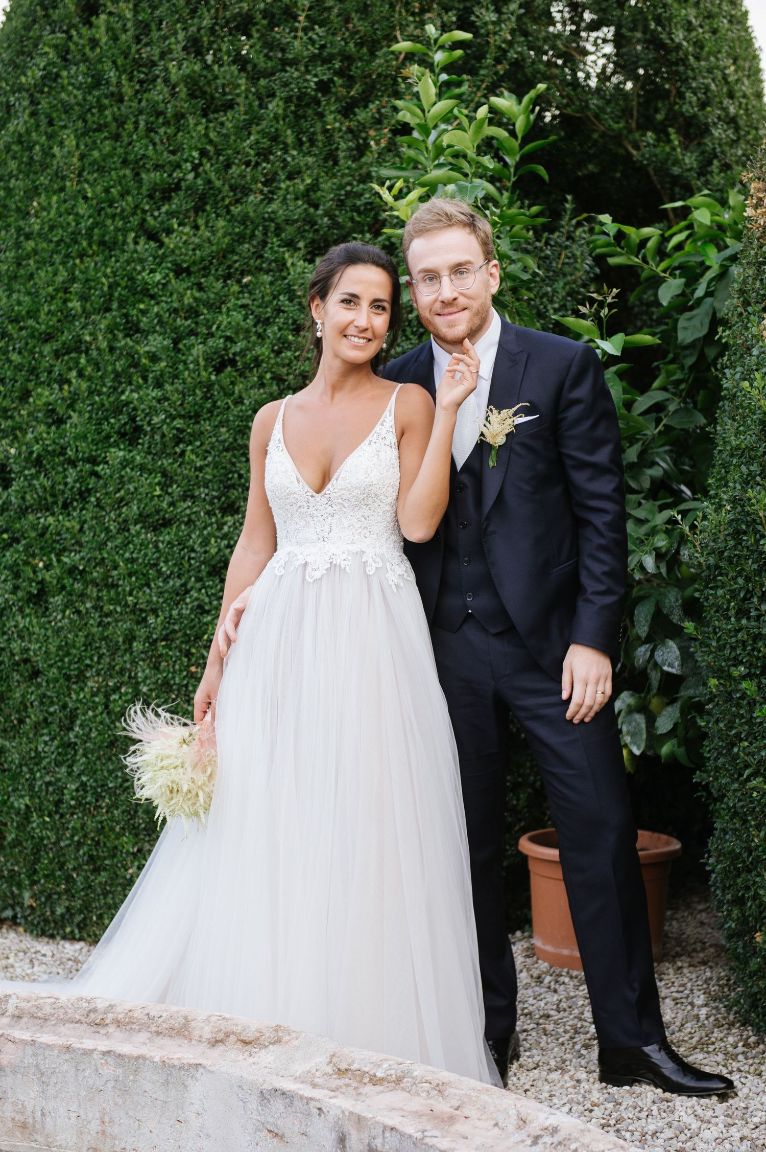 Wedding couple poses against lush green hedge garden backdrop.