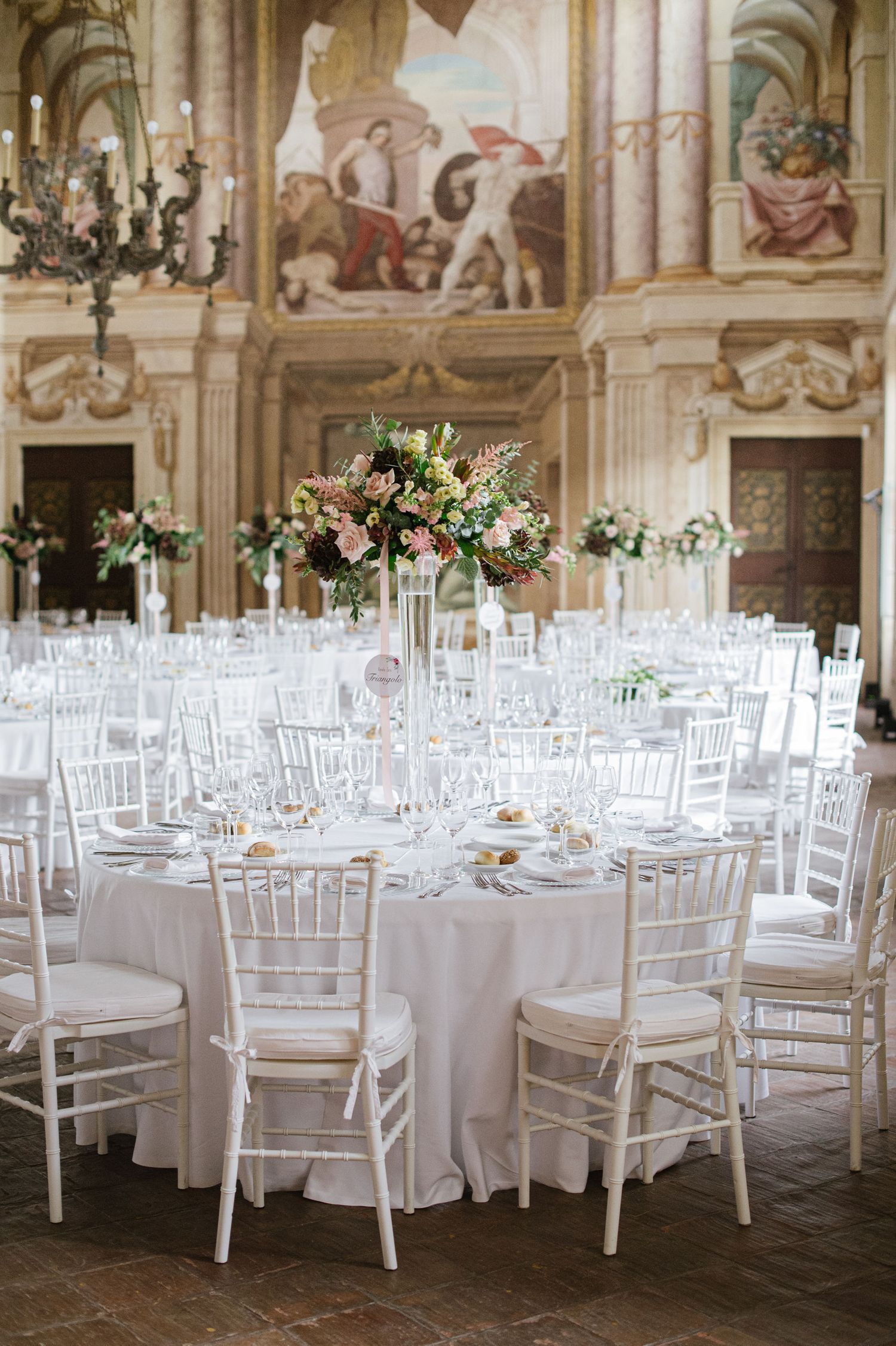 An elegant wedding reception setup with white chairs and floral centerpieces in a historic venue.