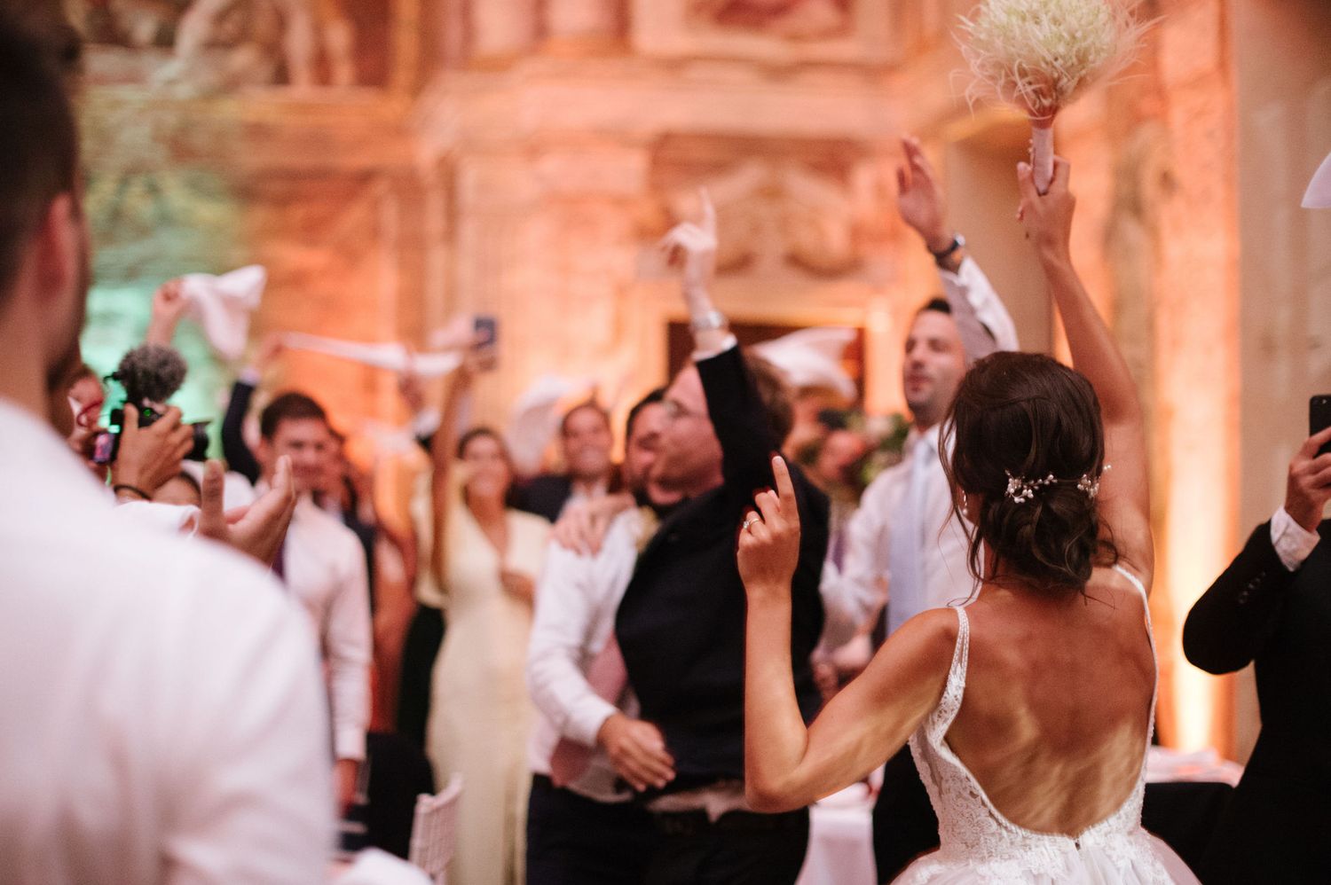Wedding celebration with guests dancing and celebrating in an ornate historic venue.