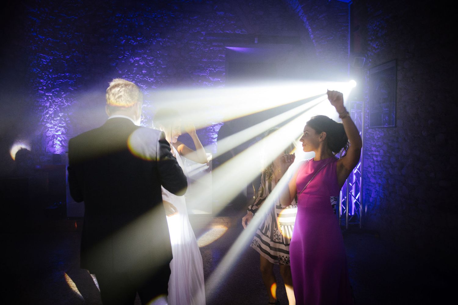 Dynamic spotlights illuminate a dark dance floor during a wedding reception.
