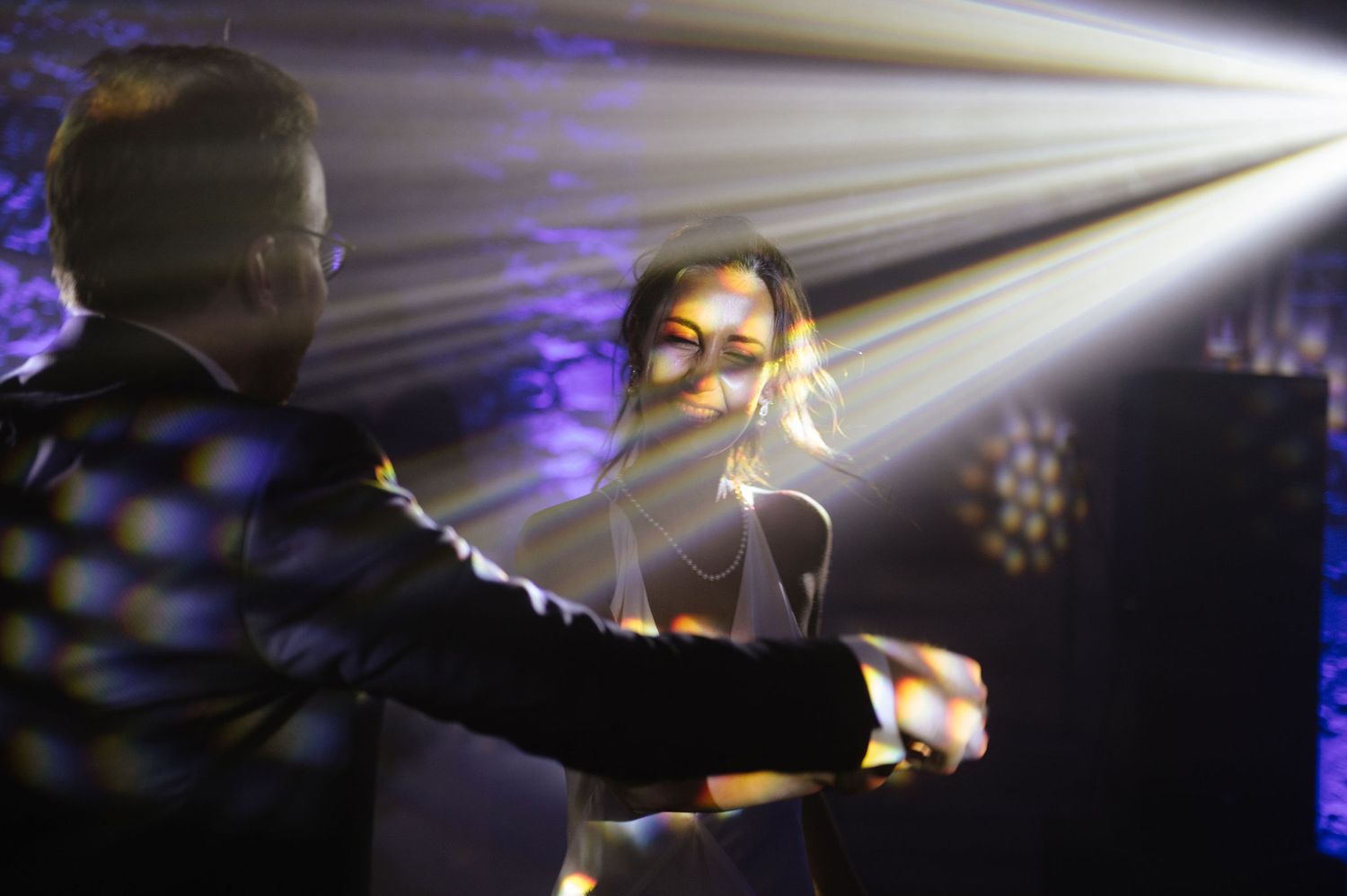 Dancing silhouettes illuminated by dramatic white spotlight beams at a reception.