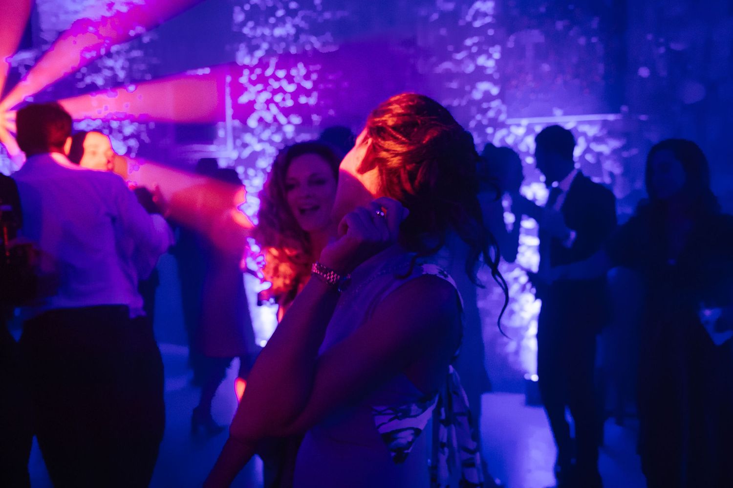 Wedding reception dance floor with vibrant purple lighting and dancing guests.