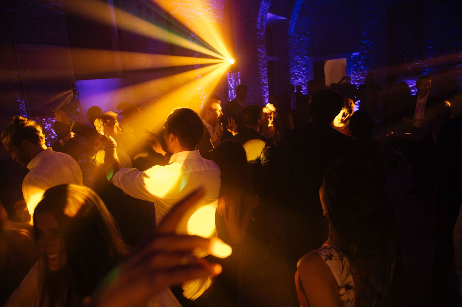 Golden spotlight rays illuminate a crowded dance floor during a celebration.