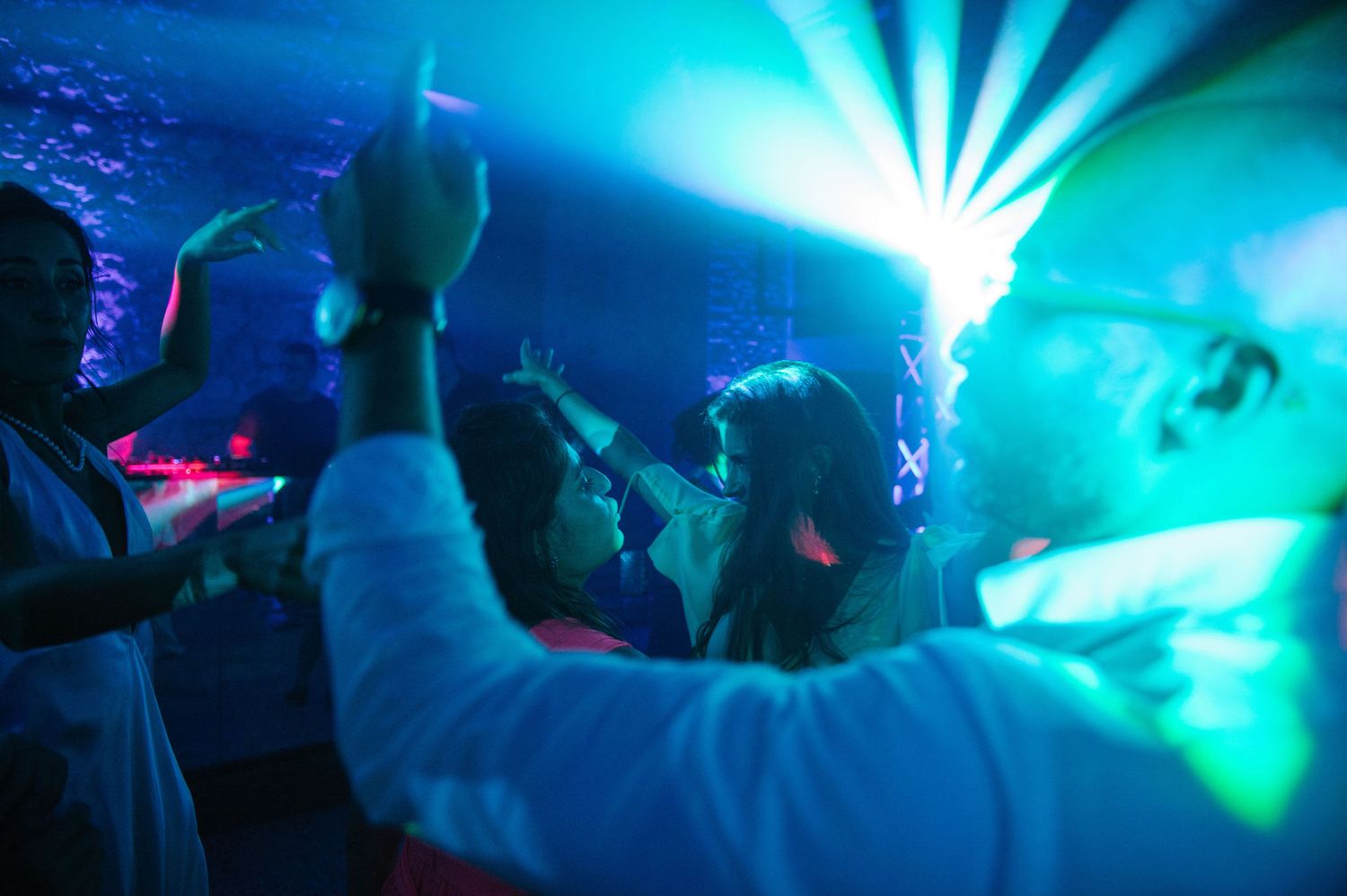 Energetic dance party scene with bright turquoise lighting and raised hands.